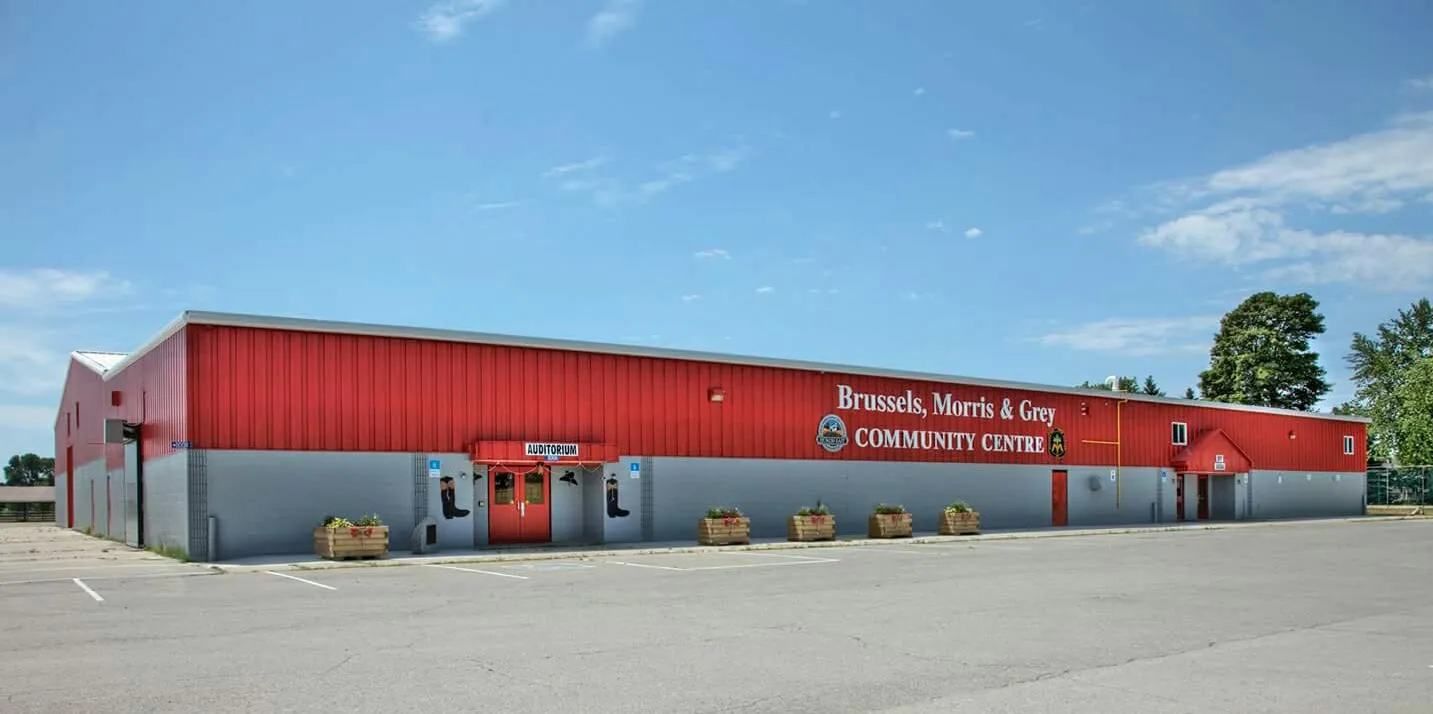 The long red and grey building with the Brussels, Morris & Grey Community Centre sign over the doors and planters along the front. — Brussels, Morris and Grey Community Centre