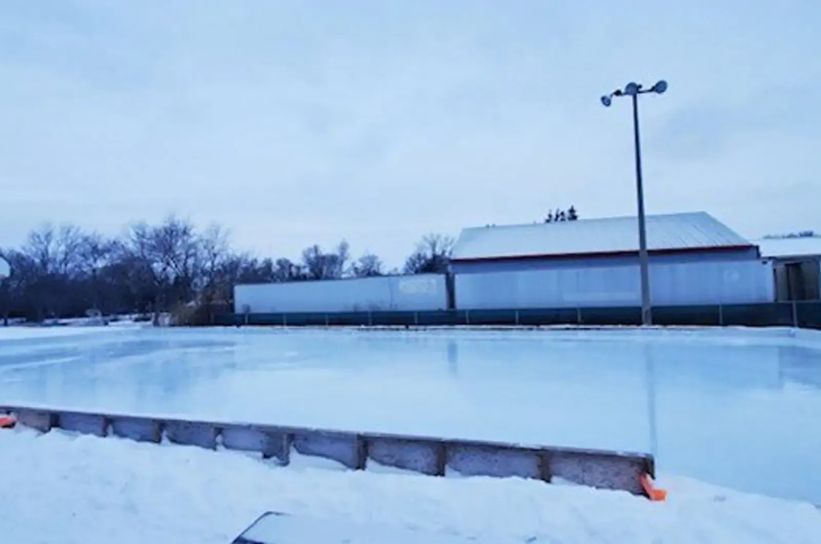 The outdoor ice rink at Bud Brown Park in Bradford West Gwillimbury, with a shelter building beside the boards. — Bud Brown Park Outdoor Rinks