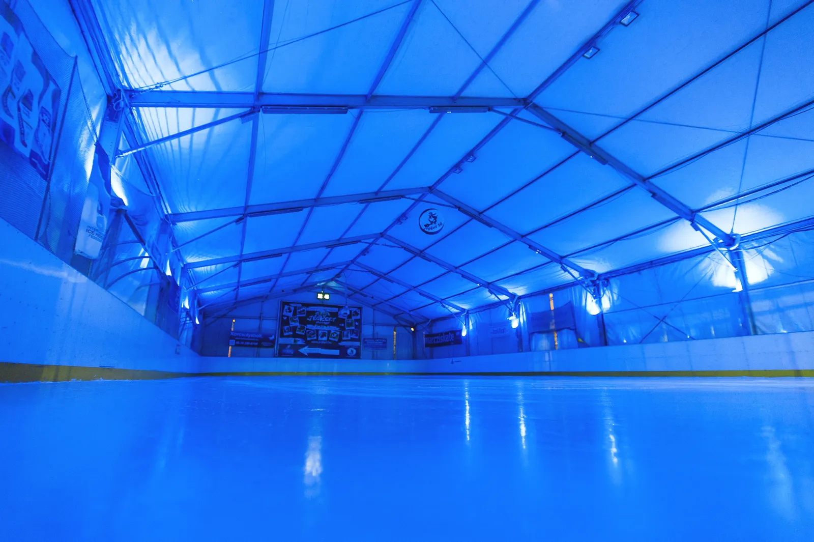 The empty ice of the covered Jégkert rink at Széna tér, lit blue — Budai Jégpálya (Jégkert)
