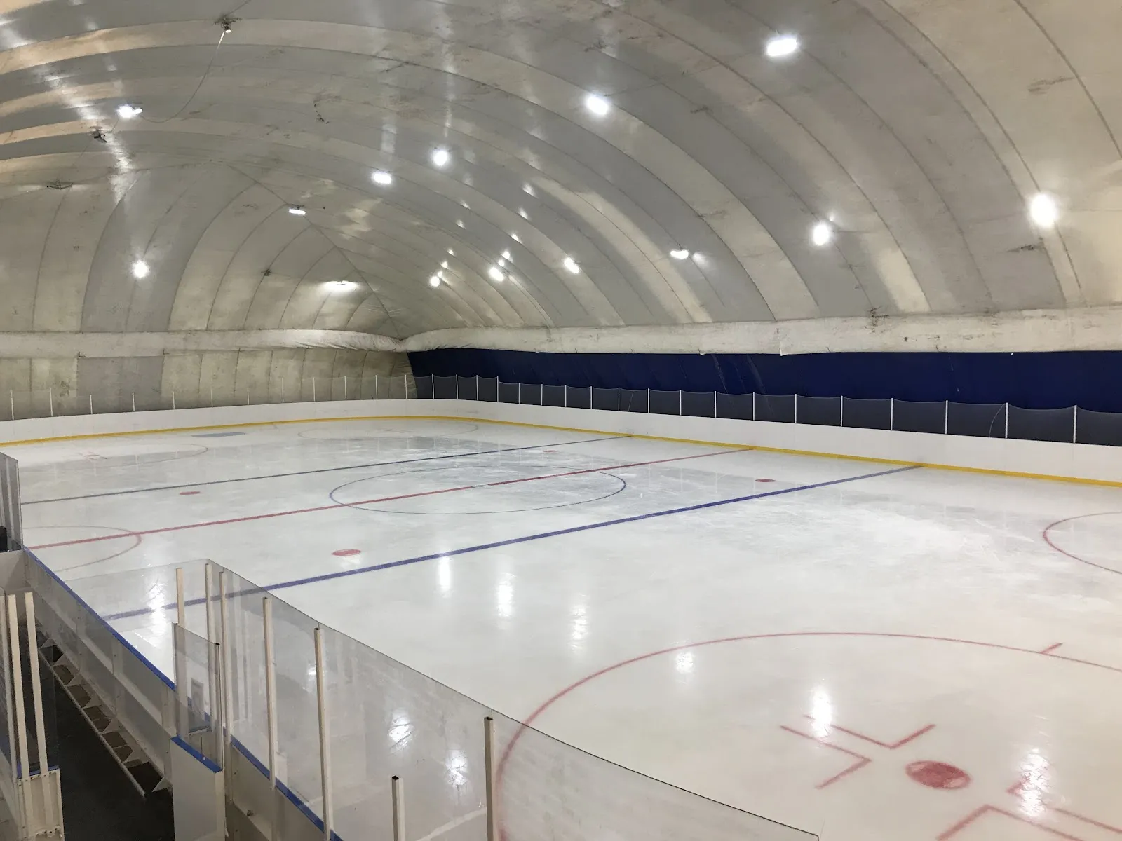 The ice sheet of the big Bugry arena under its vaulted air-dome roof, seen from the stands — Bugry Ice Arena
