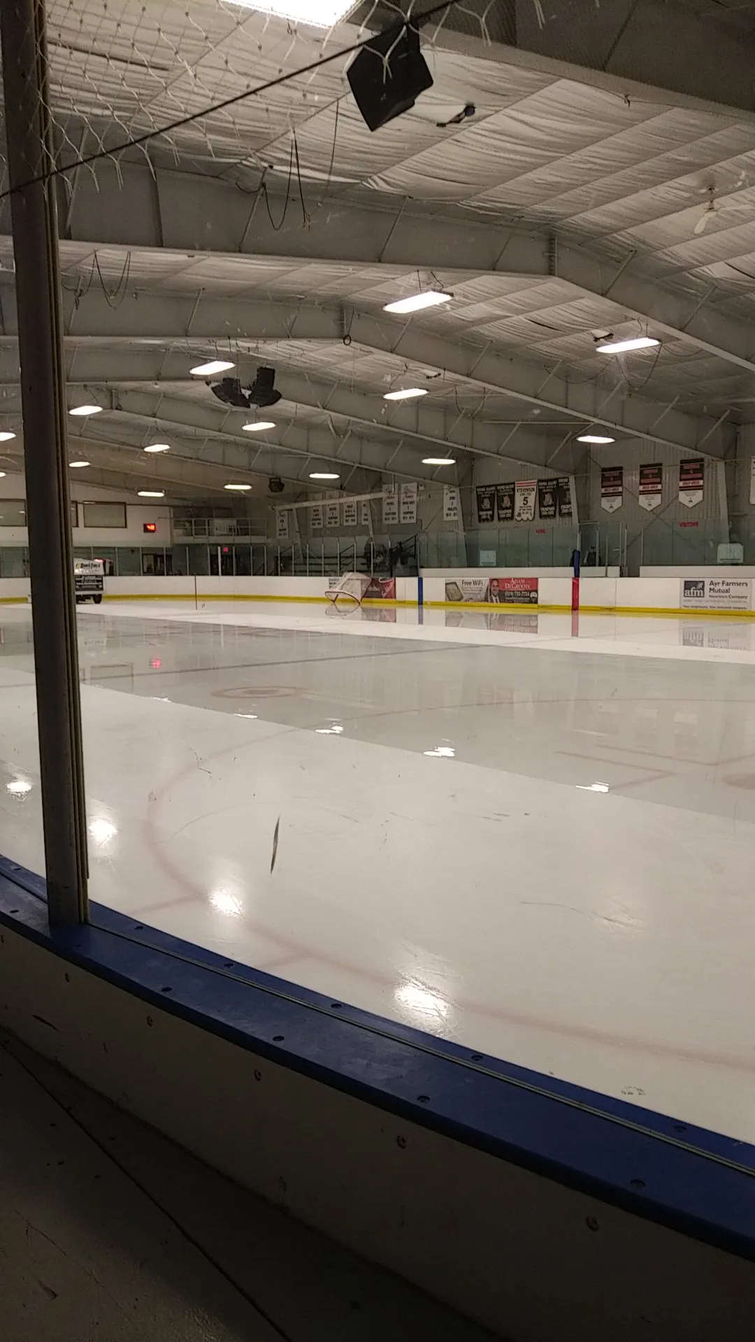 The arena ice at Burford Community Centre seen through the glass, with banners hanging from the rafters above the far boards. — Burford Community Centre