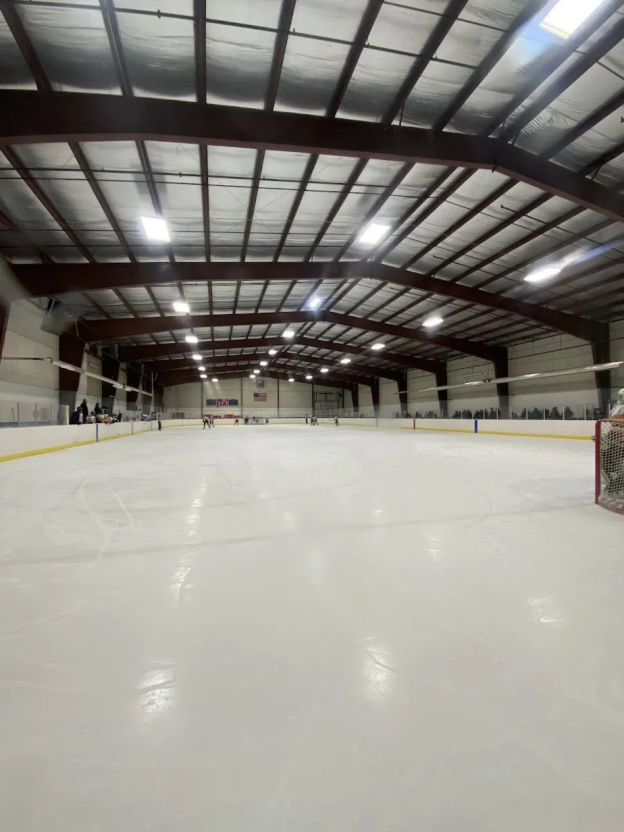 The empty sheet from rink level, stretching under the steel roof trusses and lights to the far end. — Burich Arena