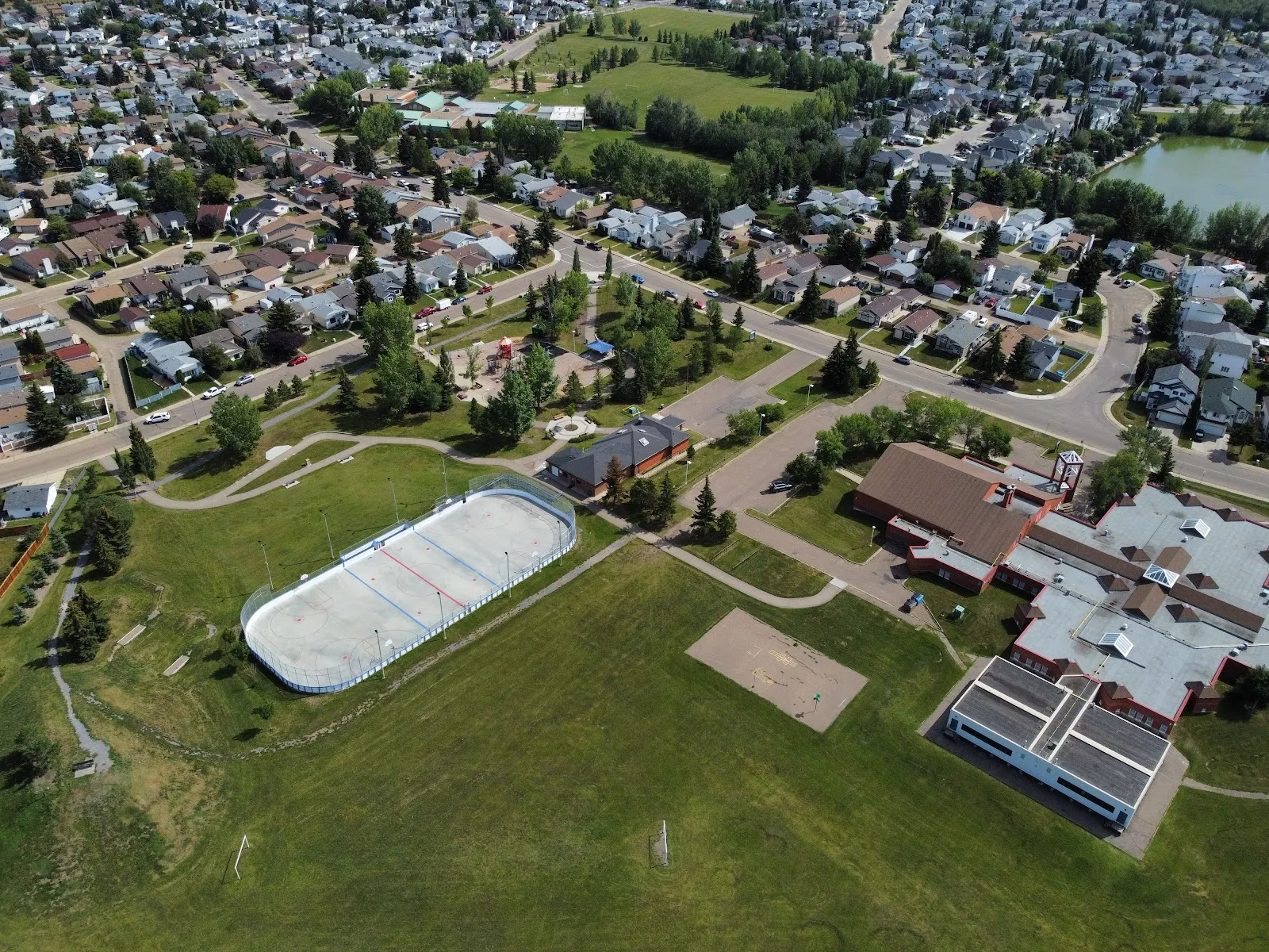 Aerial view of the Burnewood community grounds, with the boarded rink beside the hall and school fields — Burnewood Community League Rink