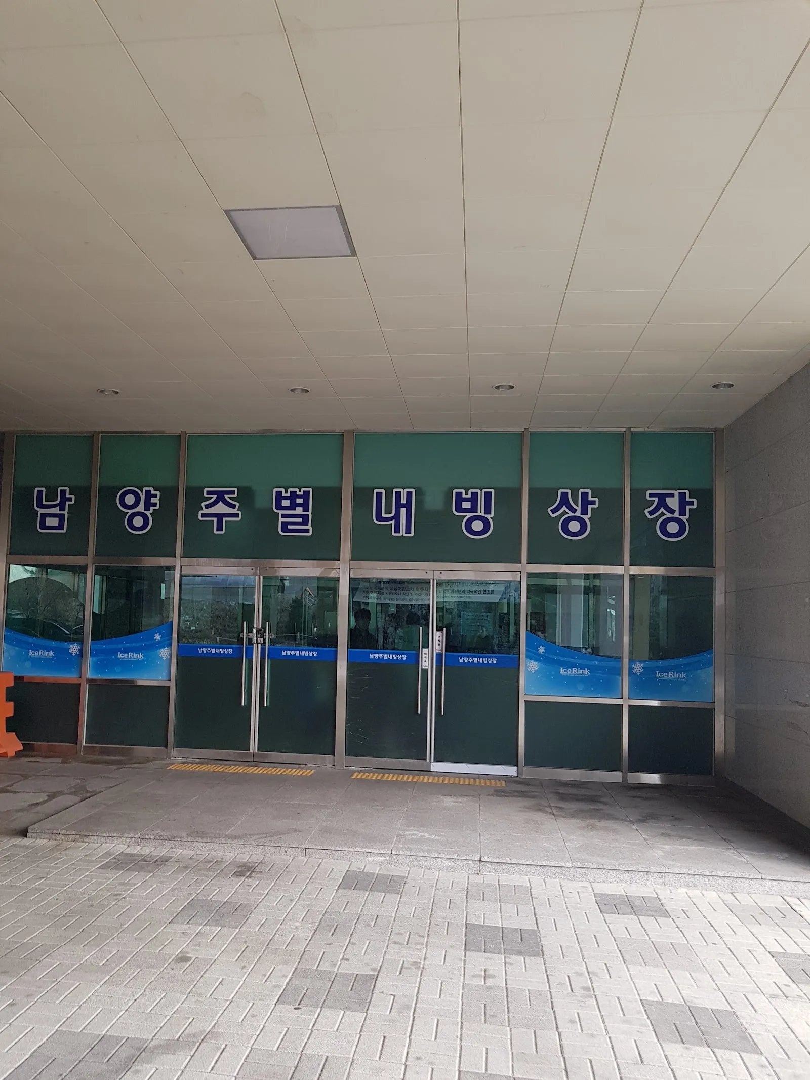 The glass entrance doors of the Namyangju Byeollae ice rink under its Hangul name sign, on a paved forecourt. — Byeollae Ice Rink (Namyangju)
