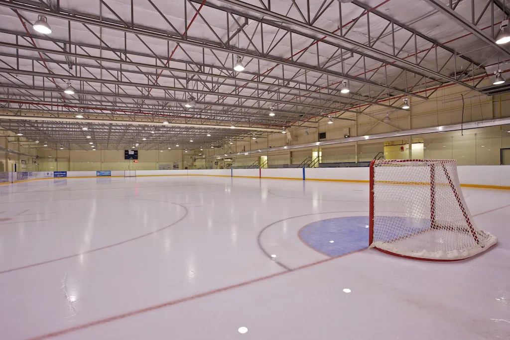 Empty ice at Murray Copot Arena, a net at the near crease under a long white steel-truss roof — Murray Copot Arena