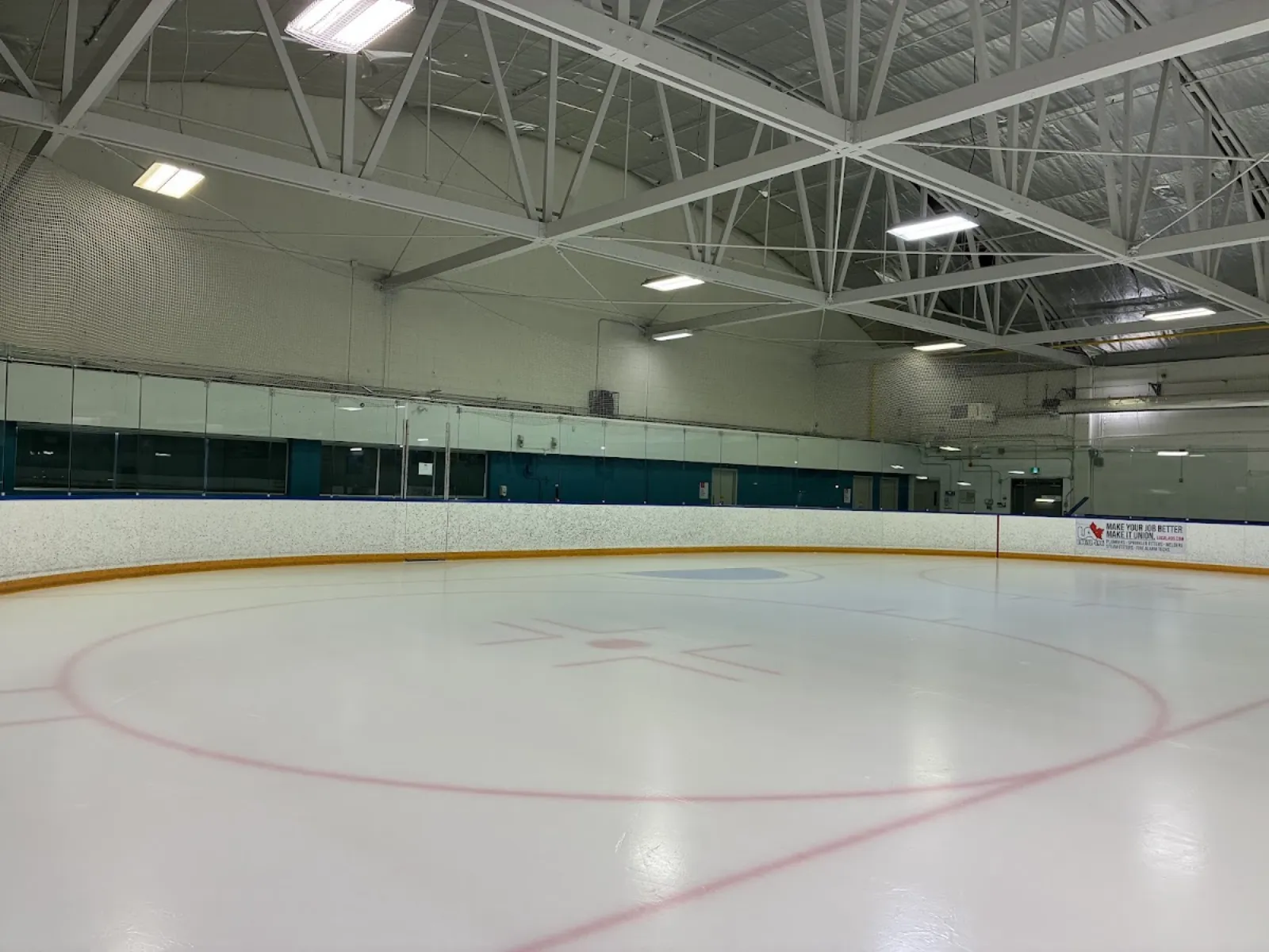 Pista de hielo techada vacía con un círculo de saque rojo, cristal a lo largo de las vallas y armaduras blancas de acero en el techo. — Rose Kohn and Jimmie Condon Arenas
