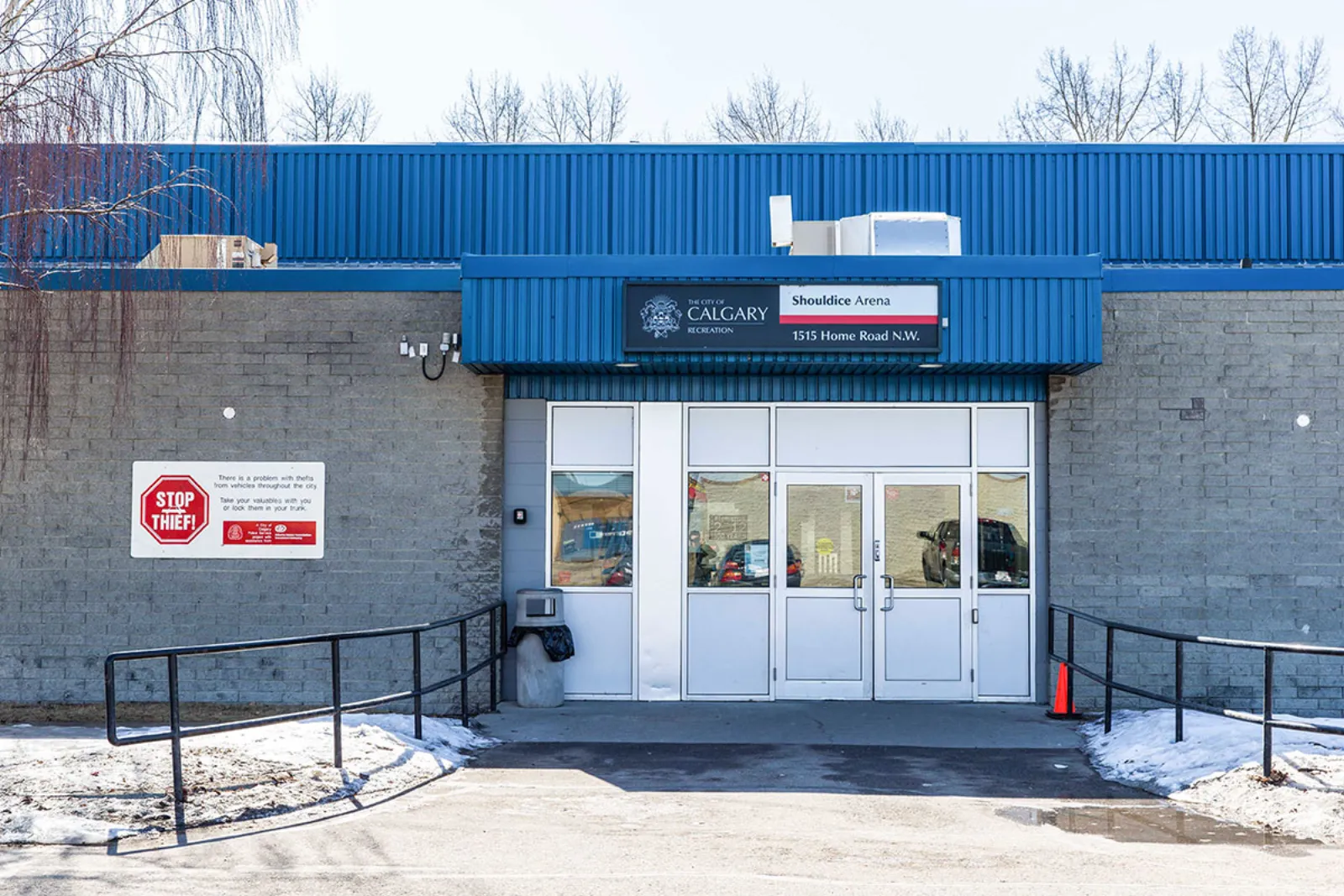 Entrada de bloques grises y paneles azules de Shouldice Arena, con un letrero iluminado que dice "The City of Calgary Recreation — Shouldice Arena, 1515 Home Road N.W." sobre las puertas. — Shouldice Arena