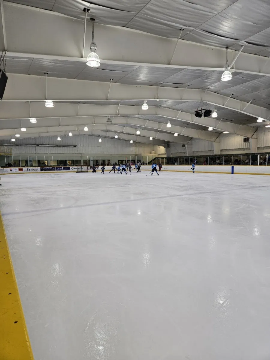 The full ice surface under the arched white roof, with a team practising at the far end. — Cambrian Arena