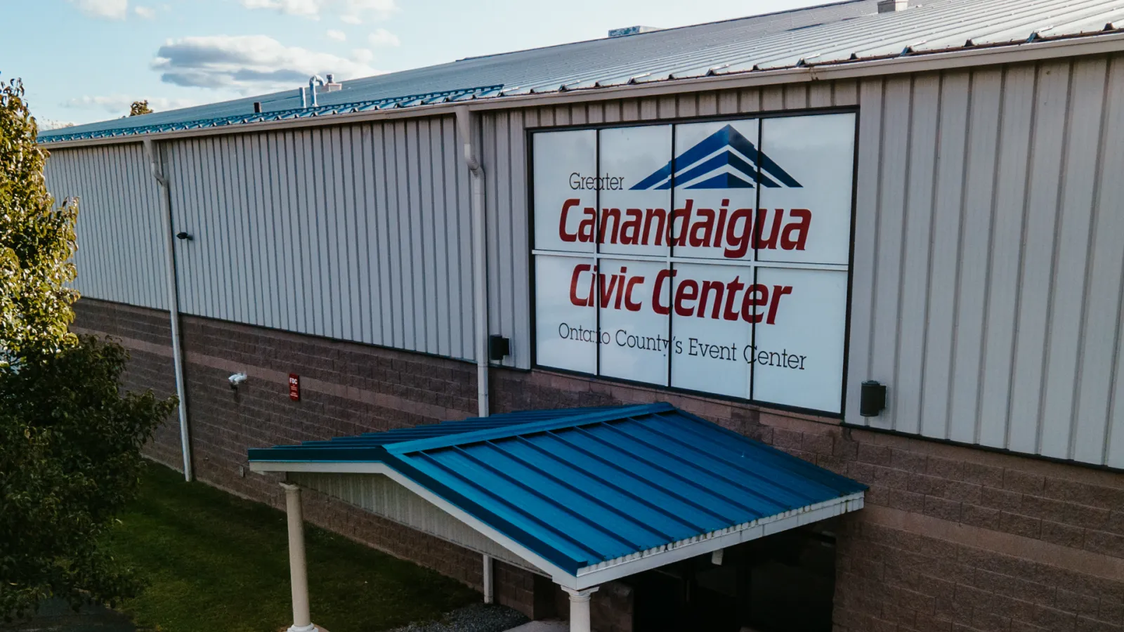 Drone view of the Civic Center's metal-sided building exterior, entrance canopy, and illuminated "Greater Canandaigua Civic Center / Ontario County's Event Center" wall sign. — Greater Canandaigua Civic Center
