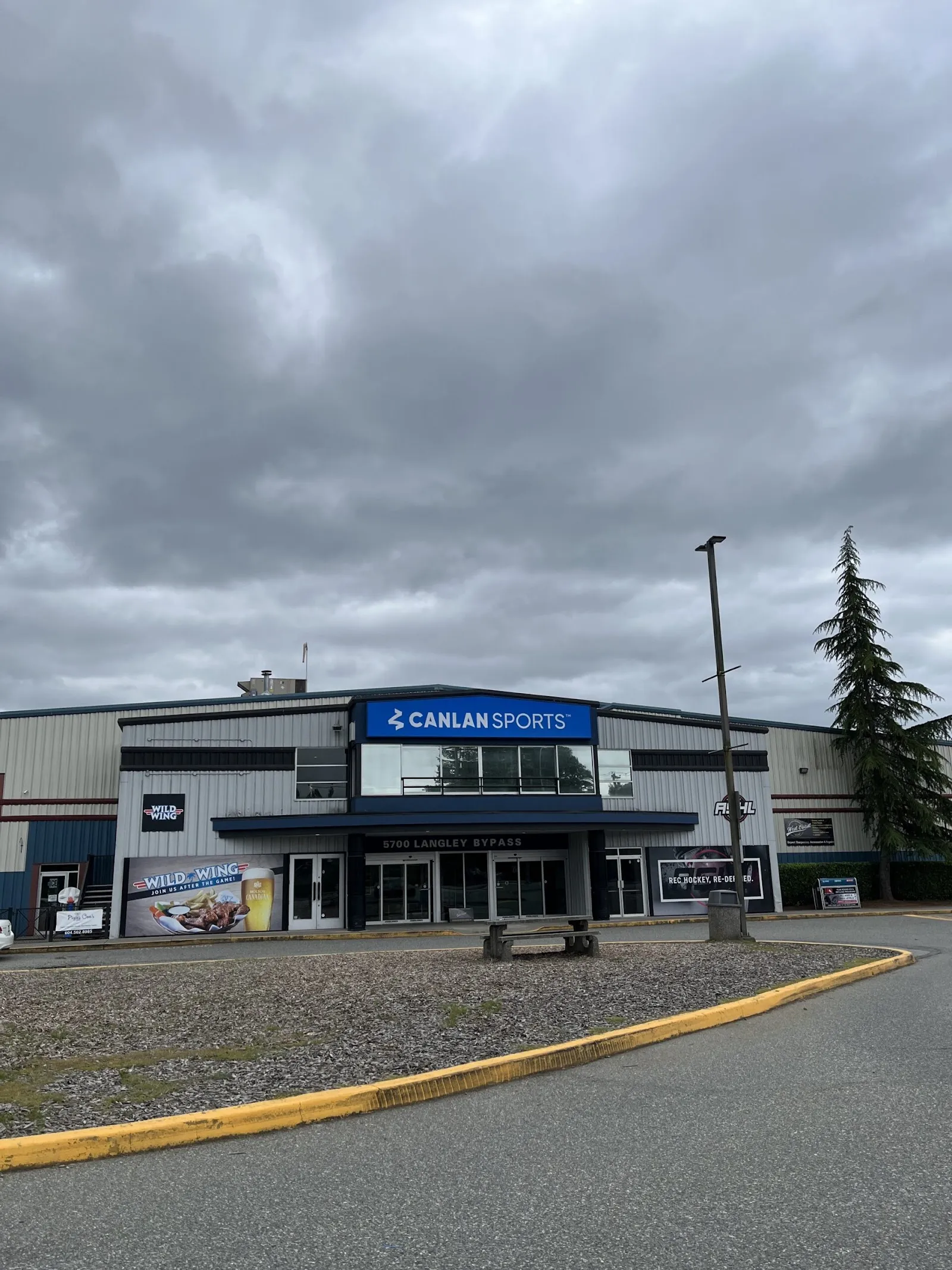 Front entrance of the Canlan Sports building at 5700 Langley Bypass, with the blue CANLAN SPORTS sign over the doors and a Wild Wing banner beside the entrance. — Canlan Sports Langley Twin Rinks