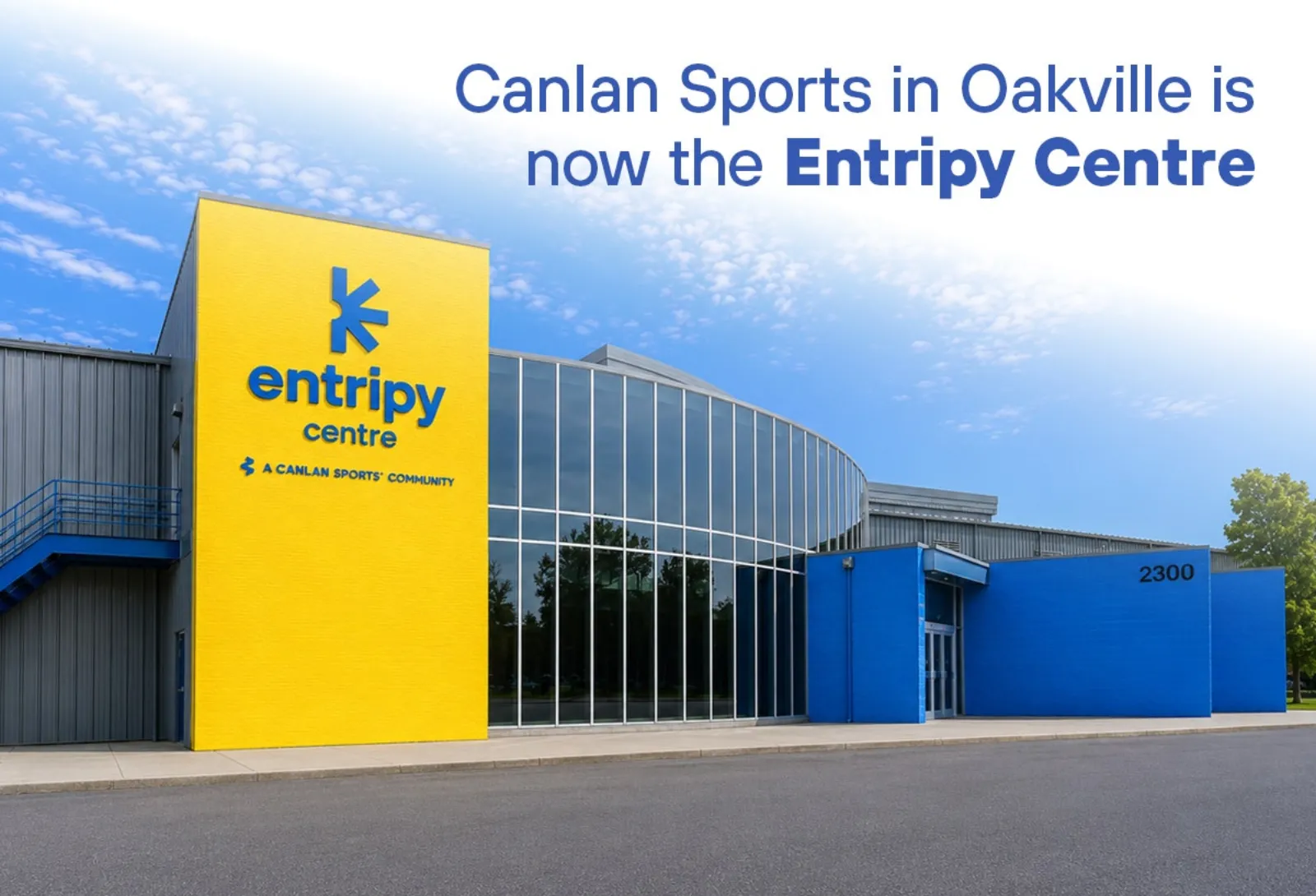 Front entrance of the Entripy Centre, a Canlan Sports community facility, showing the yellow signage tower with the Entripy Centre logo, the glass-fronted entrance, and the 2300 street number on the blue wall — Entripy Centre - Oakville