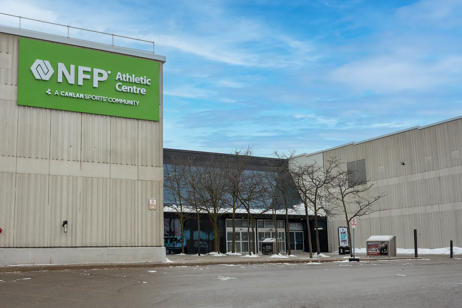 The NFP Athletic Centre entrance on a winter day, with the green "NFP Athletic Centre, a Canlan Sports community" sign on the corrugated wall and the glass lobby behind. — NFP Athletic Centre - York