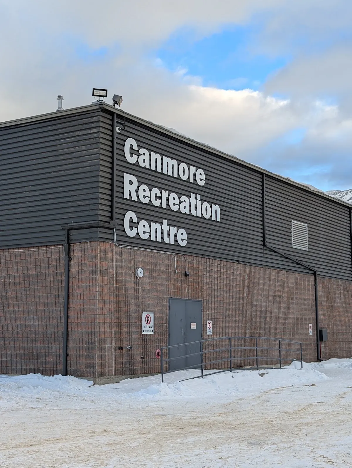 The Canmore Recreation Centre's grey-clad arena wall with the centre's name in large white letters, in winter. — Canmore Recreation Centre