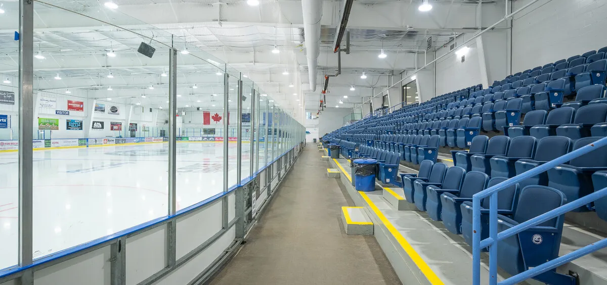 One of the Canmore Recreation Centre's two NHL-size rinks, seen along the glass beside rows of blue seats. — Canmore Recreation Centre