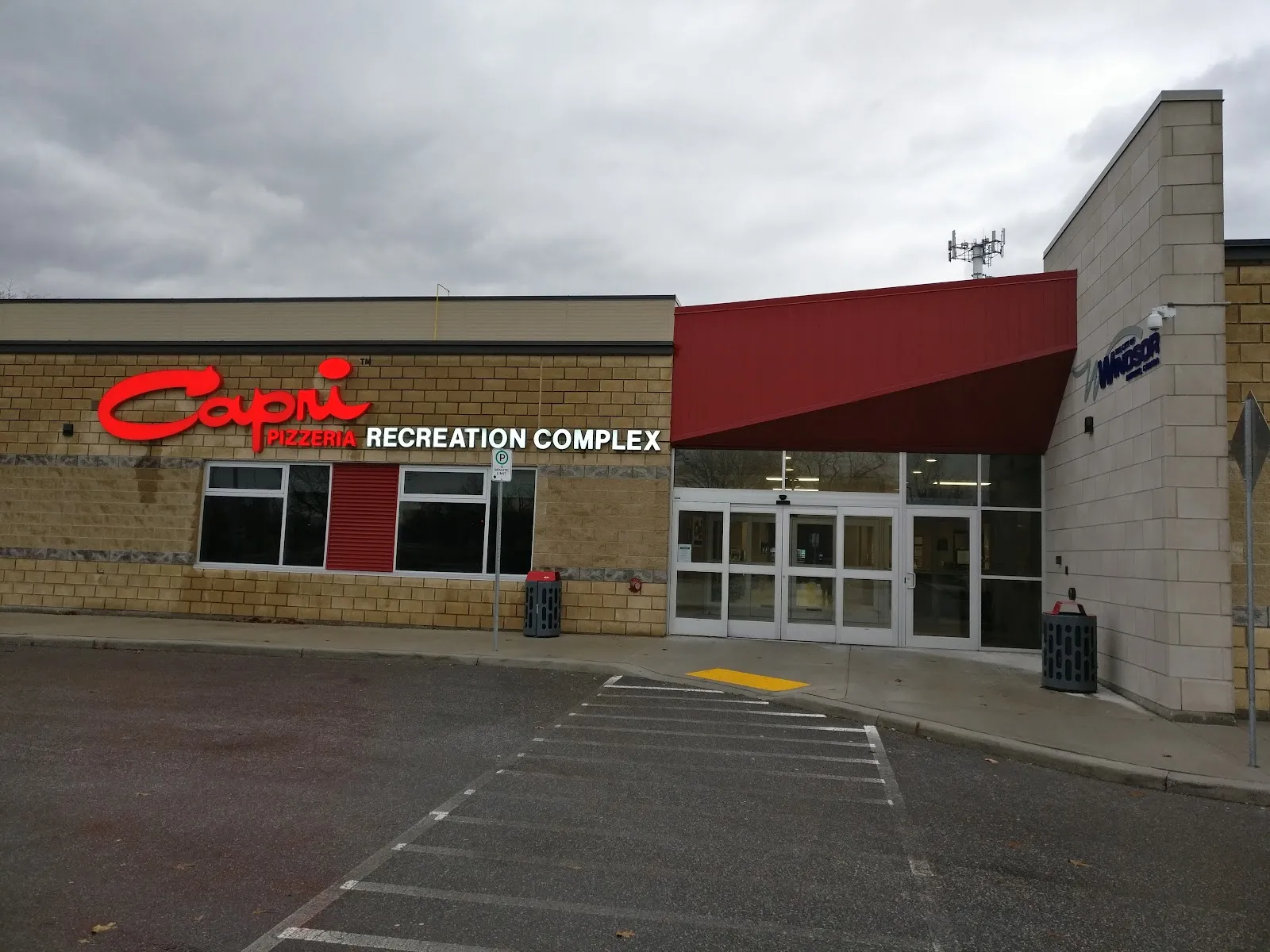 The brick entrance with the Capri Pizzeria Recreation Complex sign and a red canopy over the glass doors. — Capri Pizzeria Recreation Complex