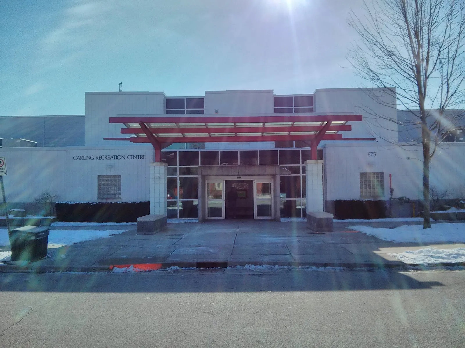 El frente del Carling Recreation Centre en 675 Grosvenor Street, con su marquesina de acero rojo sobre la entrada, bajo el sol de invierno. — Carling Arena