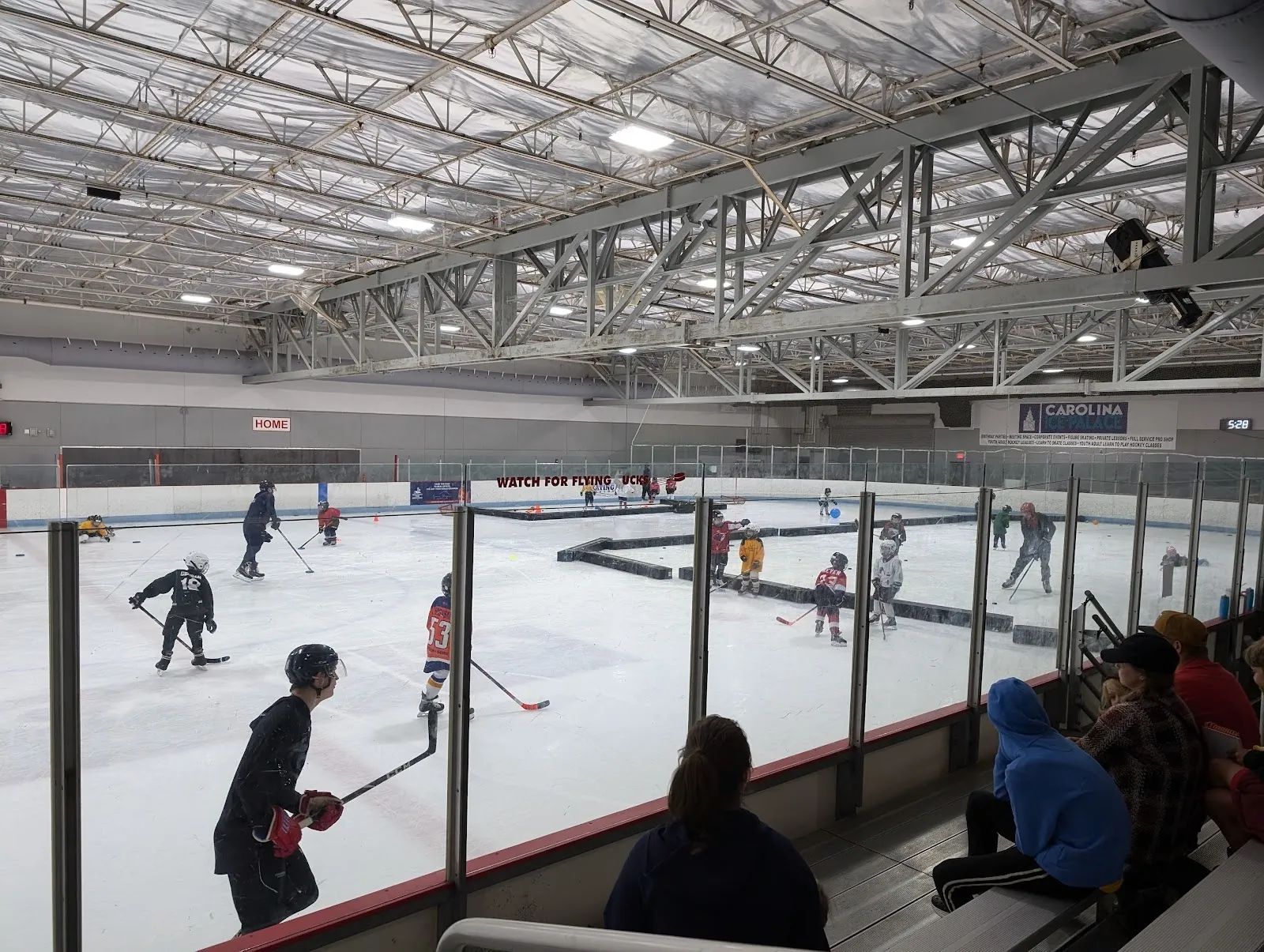 A wide view from the glass of the sheet under a long steel-trussed roof, a few skaters and players spread across the ice with benches and rink glass in front. — Carolina Ice Palace