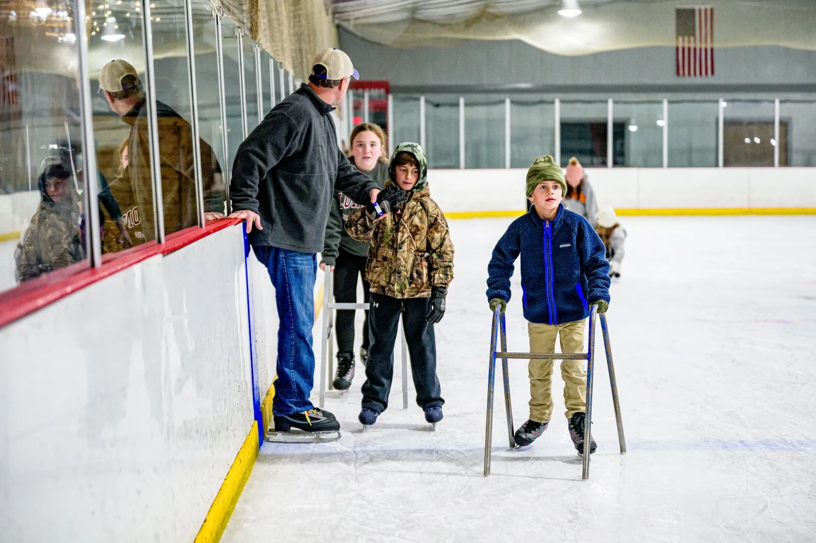 Niños patinando en una sesión pública a lo largo de las vallas, uno de ellos con un apoyo para patinar, en una foto del sitio web de la pista. — Carolina IceZone