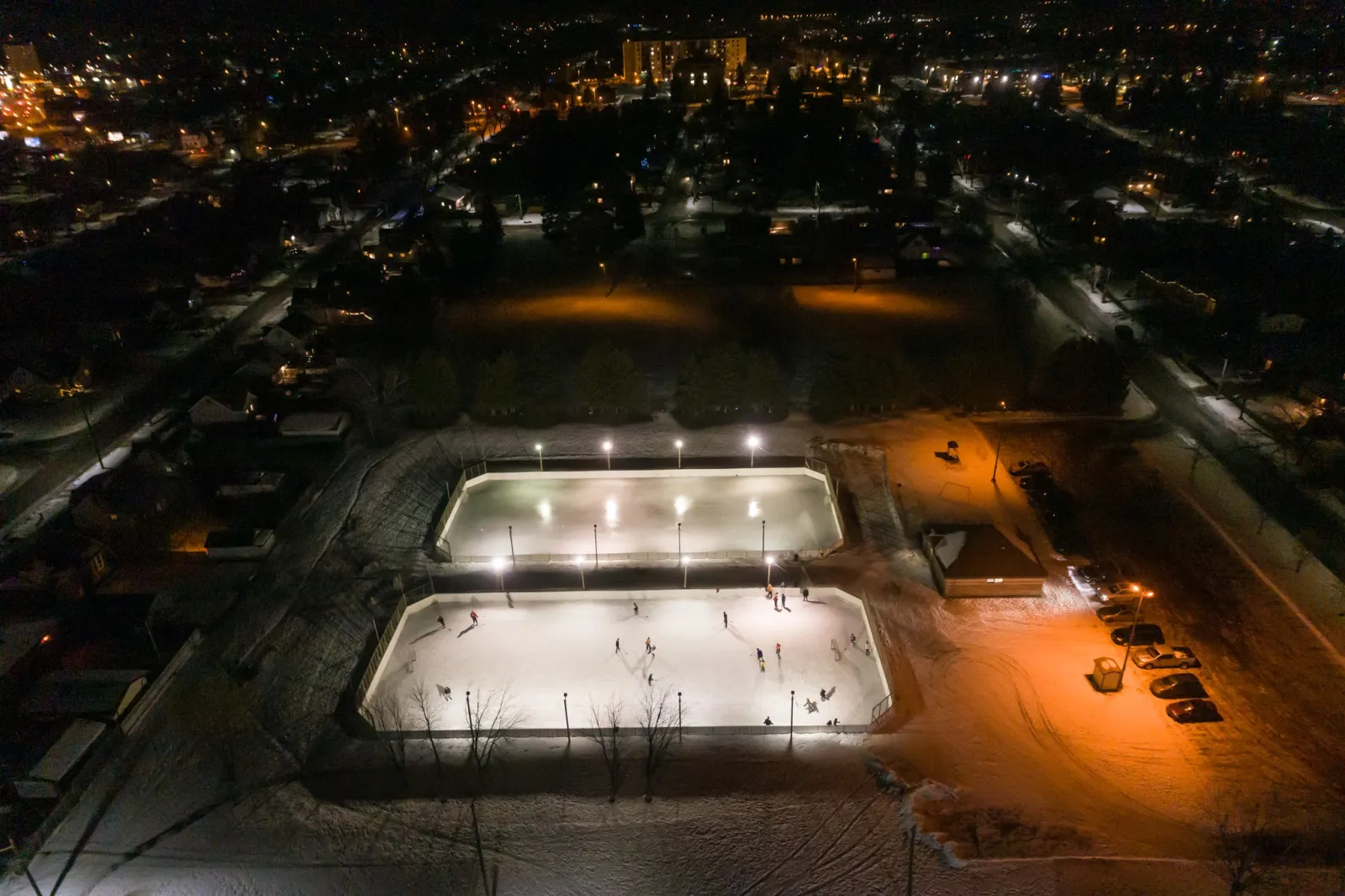 Aerial view of Carrick Park's two lit rinks with the parking lot and neighbouring streets — Carrick Park Outdoor Rinks