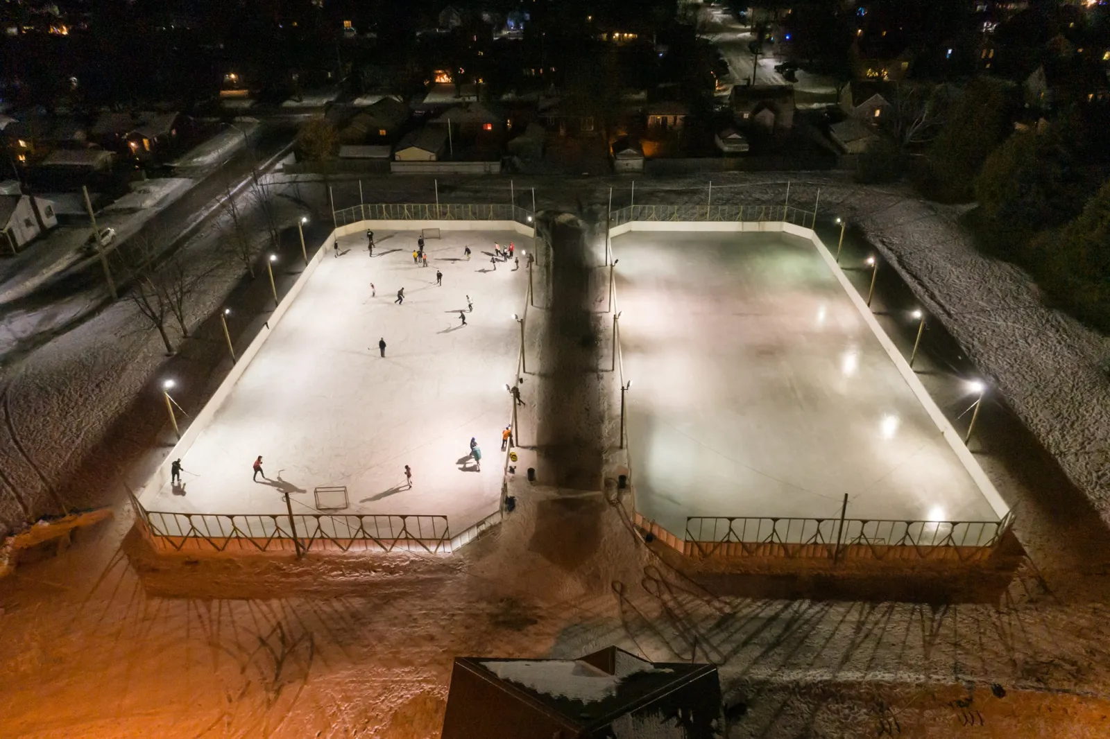 Carrick Park's two boarded rinks lit at night, seen from above, with skaters on the ice — Carrick Park Outdoor Rinks