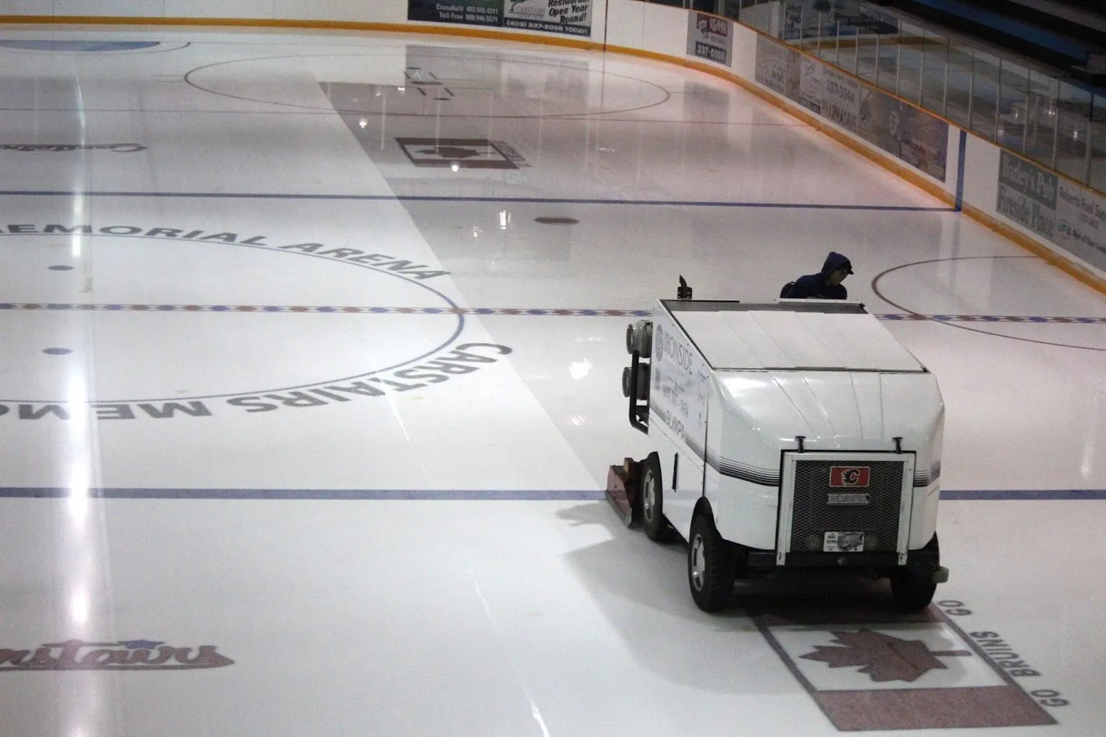 An ice resurfacer crossing the Carstairs Memorial Arena ice past the centre-ice arena logo. — Carstairs Memorial Arena