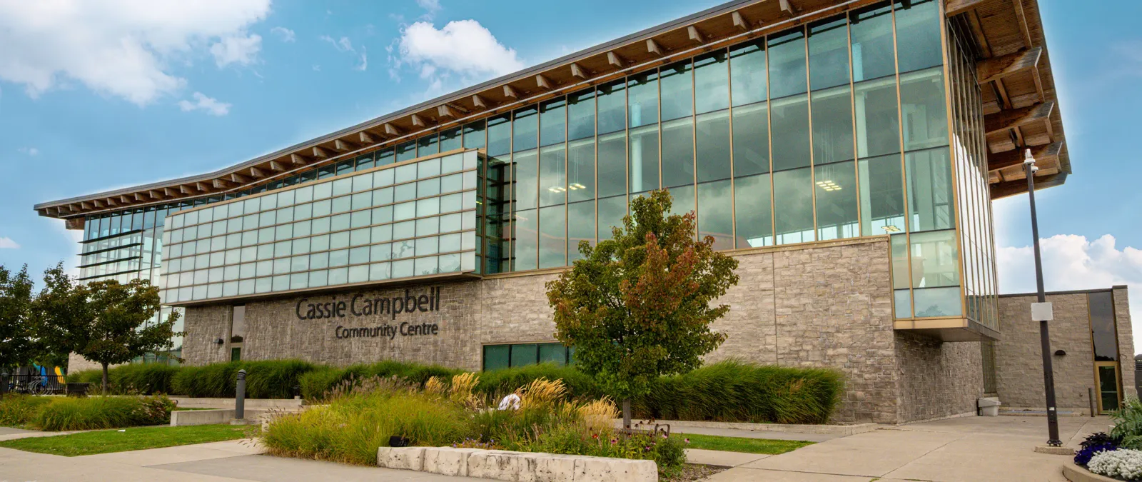 El Cassie Campbell Community Centre, con su nombre en letras sobre una base de piedra, bajo un piso superior de vidrio y un largo techo con bordes de madera. — Cassie Campbell Community Centre