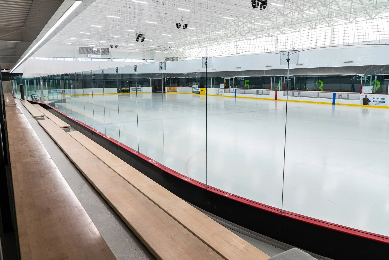 El hielo de tamaño NHL visto a lo largo del vidrio desde las bancas de madera, con la pista para caminar arriba. — Cavan Monaghan Community Centre (Millbrook)