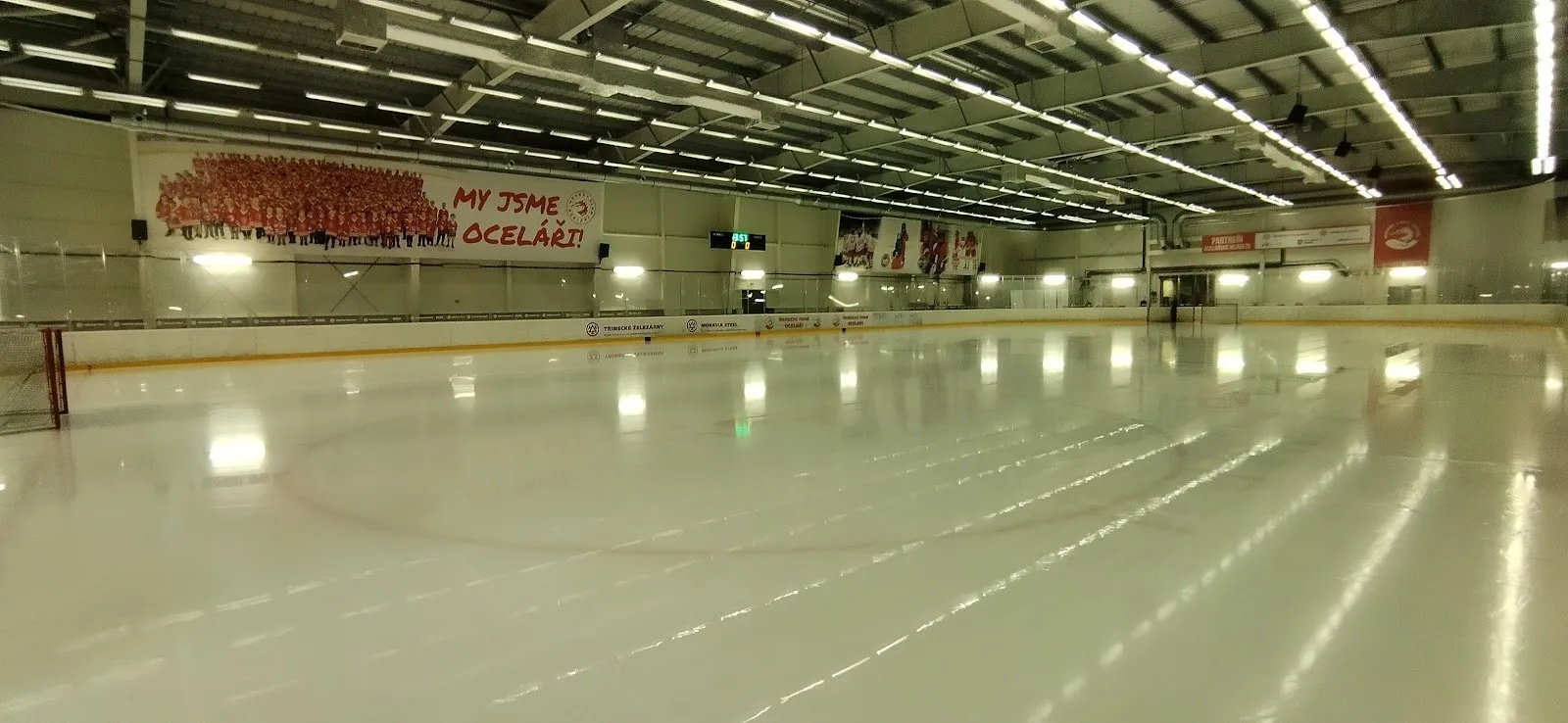 The empty ice sheet inside the CCM Aréna in Třinec, lit from the roof, with the boards and the stand behind. — CCM Aréna Třinec