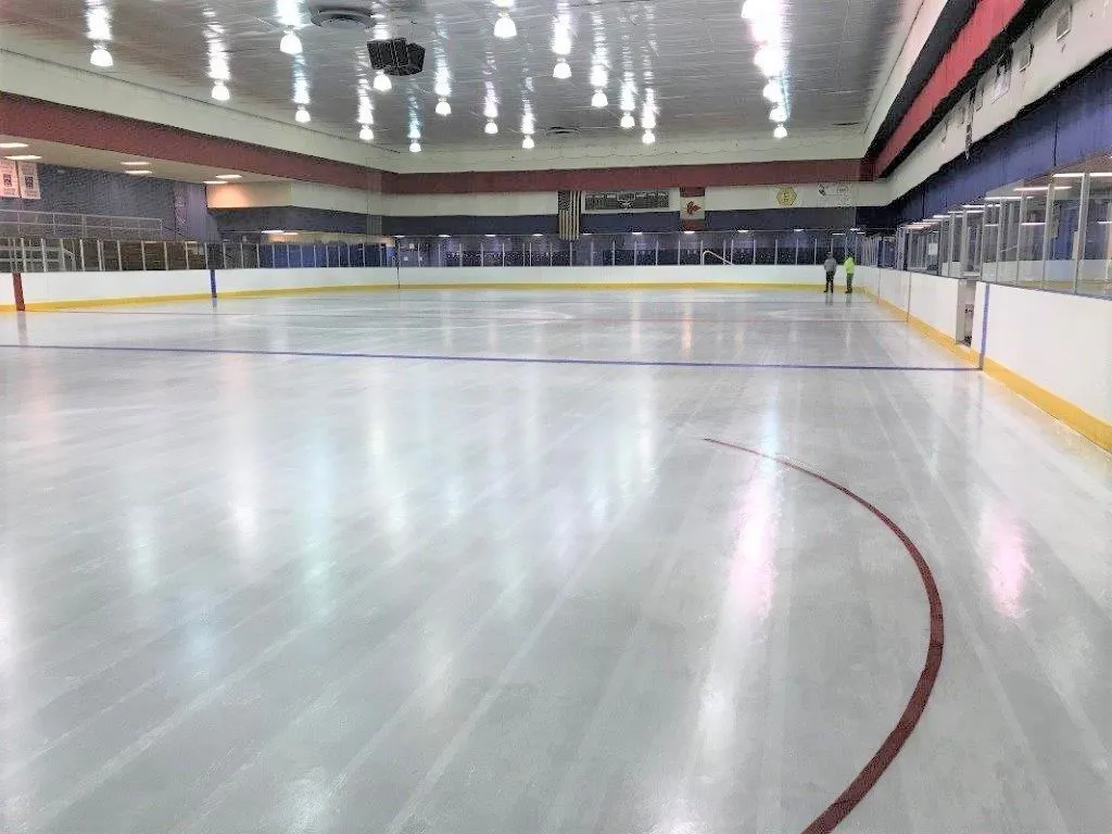 La pista vacía de C.E. Orr bajo luces brillantes, con una línea roja sobre el hielo recién hecho y las paredes rojas, blancas y azules alrededor. — C.E. Orr Ice Arena