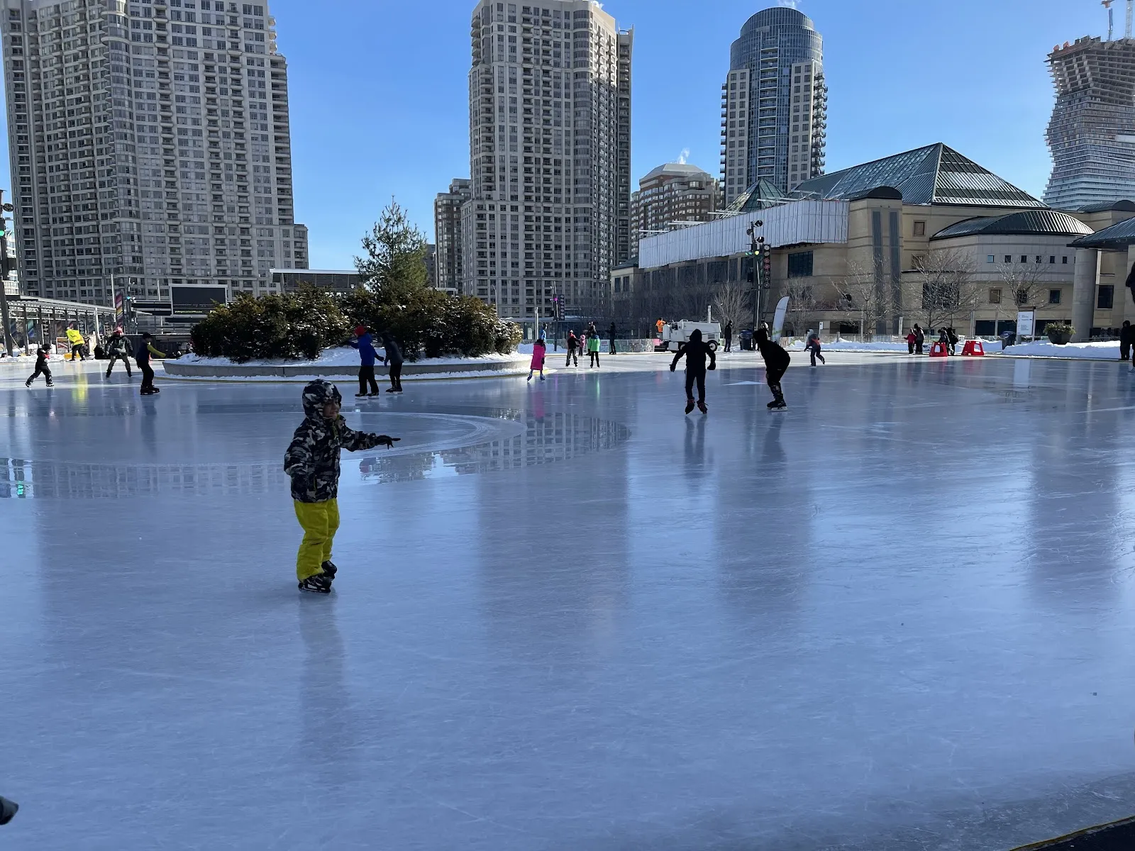Skaters on the Celebration Square rink on a bright winter day with Mississauga's condominium towers and the civic centre behind — Celebration Square Ice Rink