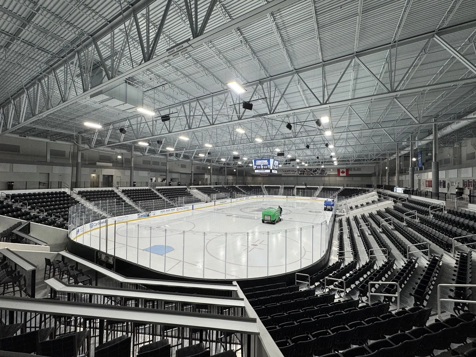 The arena bowl from the upper concourse, a resurfacer on the empty sheet below ringed by dark grandstand seating under a steel-trussed roof. — Centene Community Ice Center
