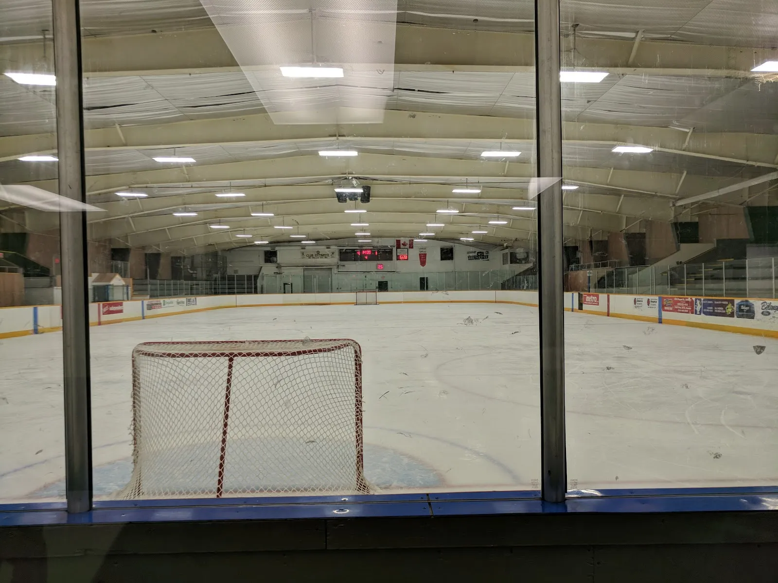 El hielo vacío visto a través del vidrio del vestíbulo, con una portería en primer plano y las gradas al fondo. — Centennial Community Centre and Arena (Hanmer)