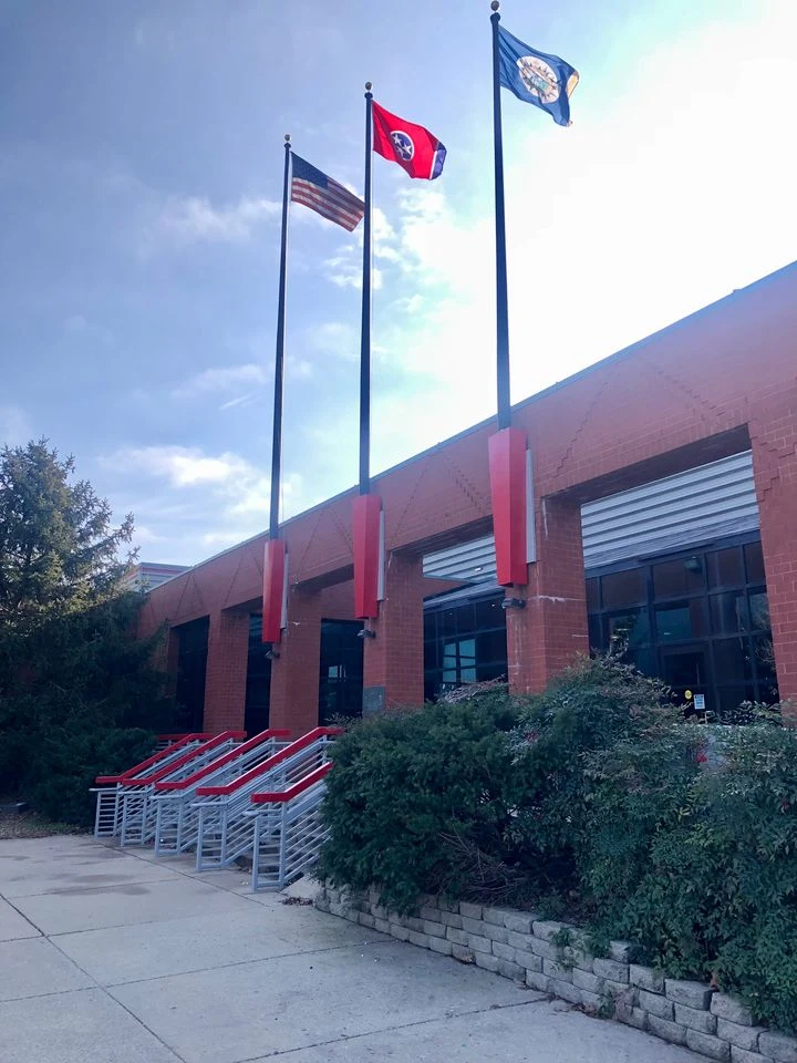 La entrada de ladrillo rojo del Sportsplex, con escalones y tres astas de bandera (2022) — Centennial Sportsplex Ice Arena