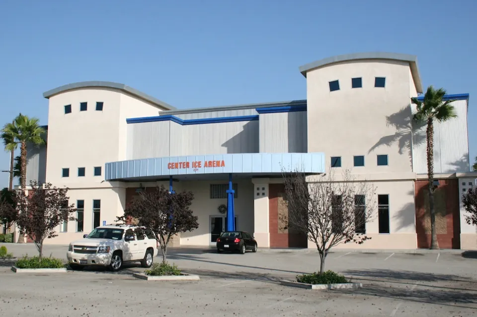 The cream stucco building with two rounded towers and a blue entrance canopy lettered Center Ice Arena, with palms and parked cars in front. — Ontario Center Ice Arena
