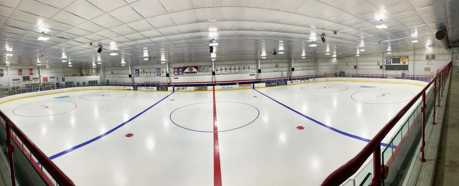 A wide panorama of the ice from one end, centre and blue lines and faceoff circles under a white roof with a red-railed walkway along the right-hand side. — Center Ice Sports Complex (North Canton)