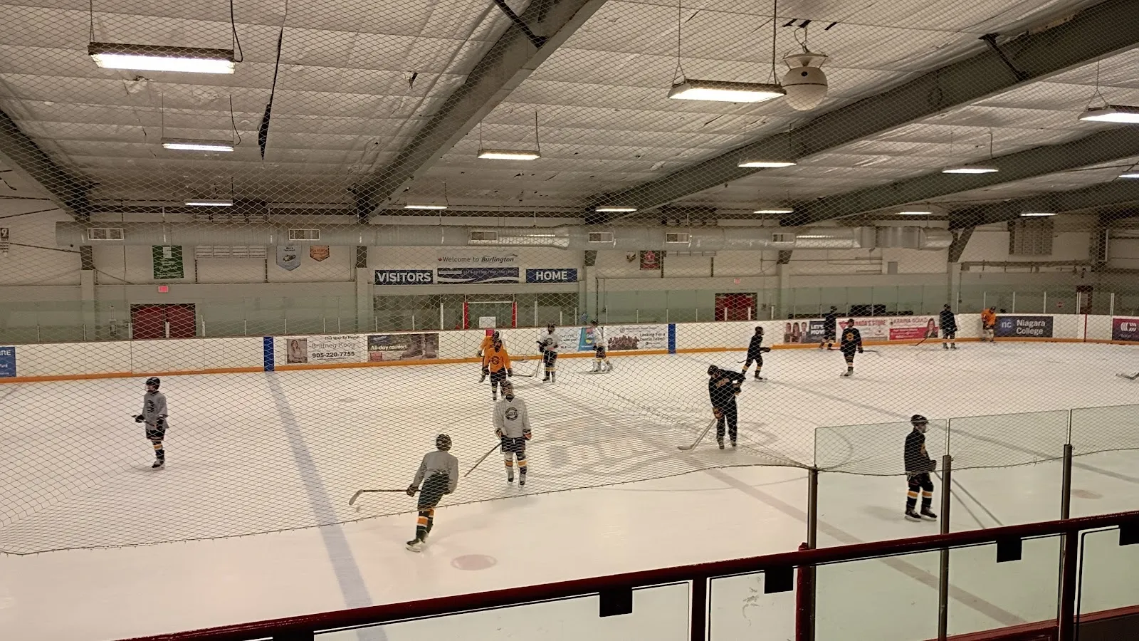 Una práctica en una pista amplia, con jugadores repartidos por el hielo entre conos bajo un techo gris con refuerzos de acero y el vidrio de la pista al frente. — Central Arena (Burlington)