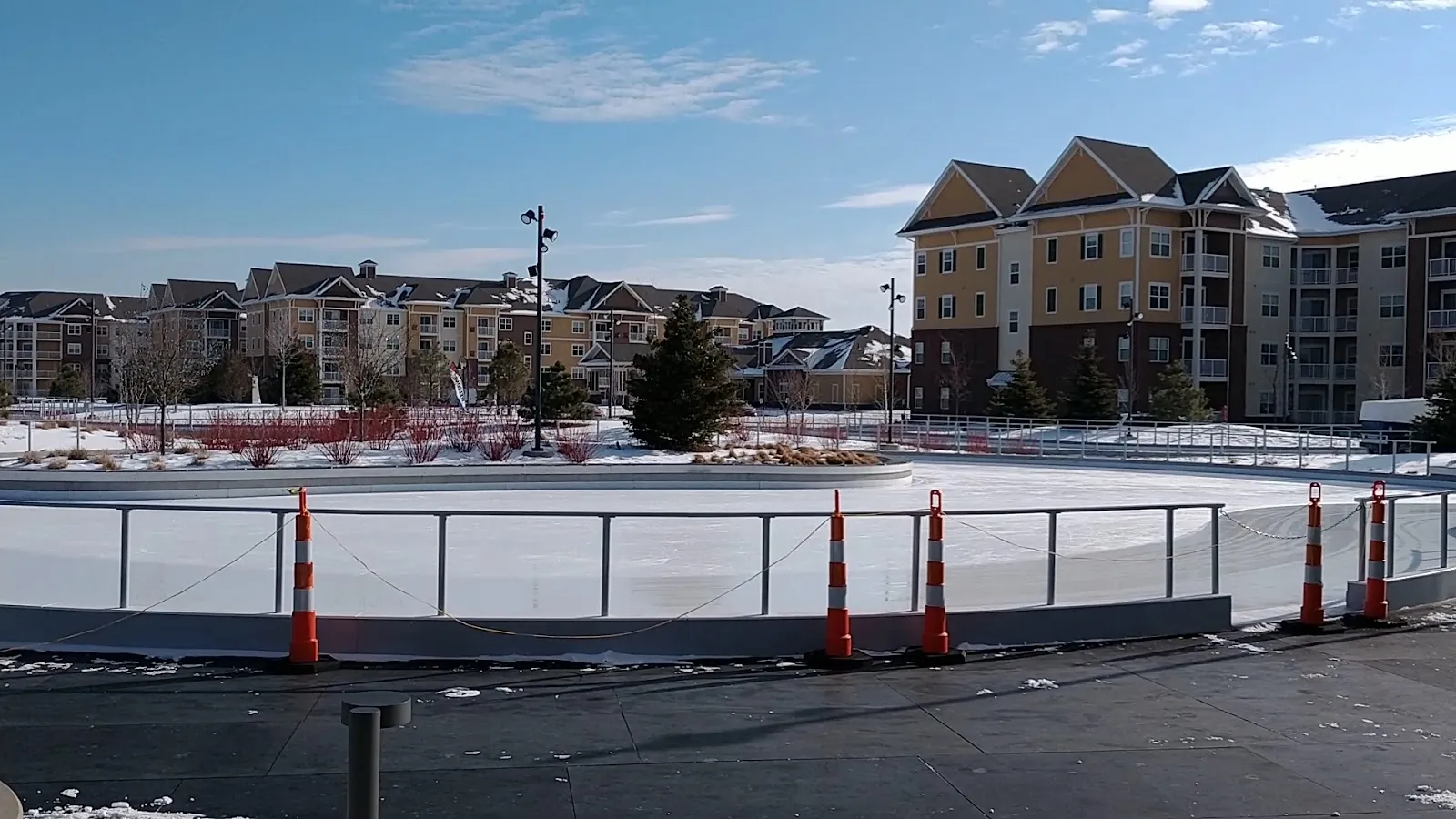 El circuito de patinaje vacío en un día despejado, con su barandal y conos de tránsito a lo largo del hielo y edificios de departamentos más allá del parque. — Central Park Ice Skating Loop