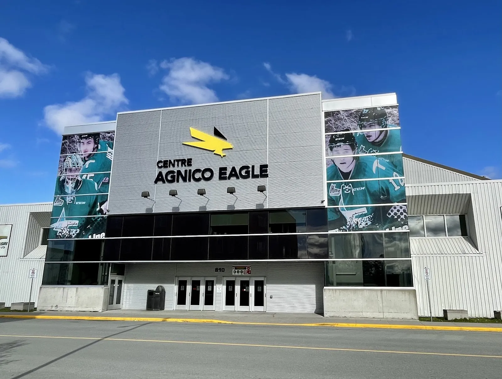 La façade de verre et de métal du Centre Agnico Eagle de Val-d’Or, avec son logo d’aigle jaune et de grandes bannières de joueurs au-dessus des portes. — Centre Agnico Eagle et Aréna Kiwanis
