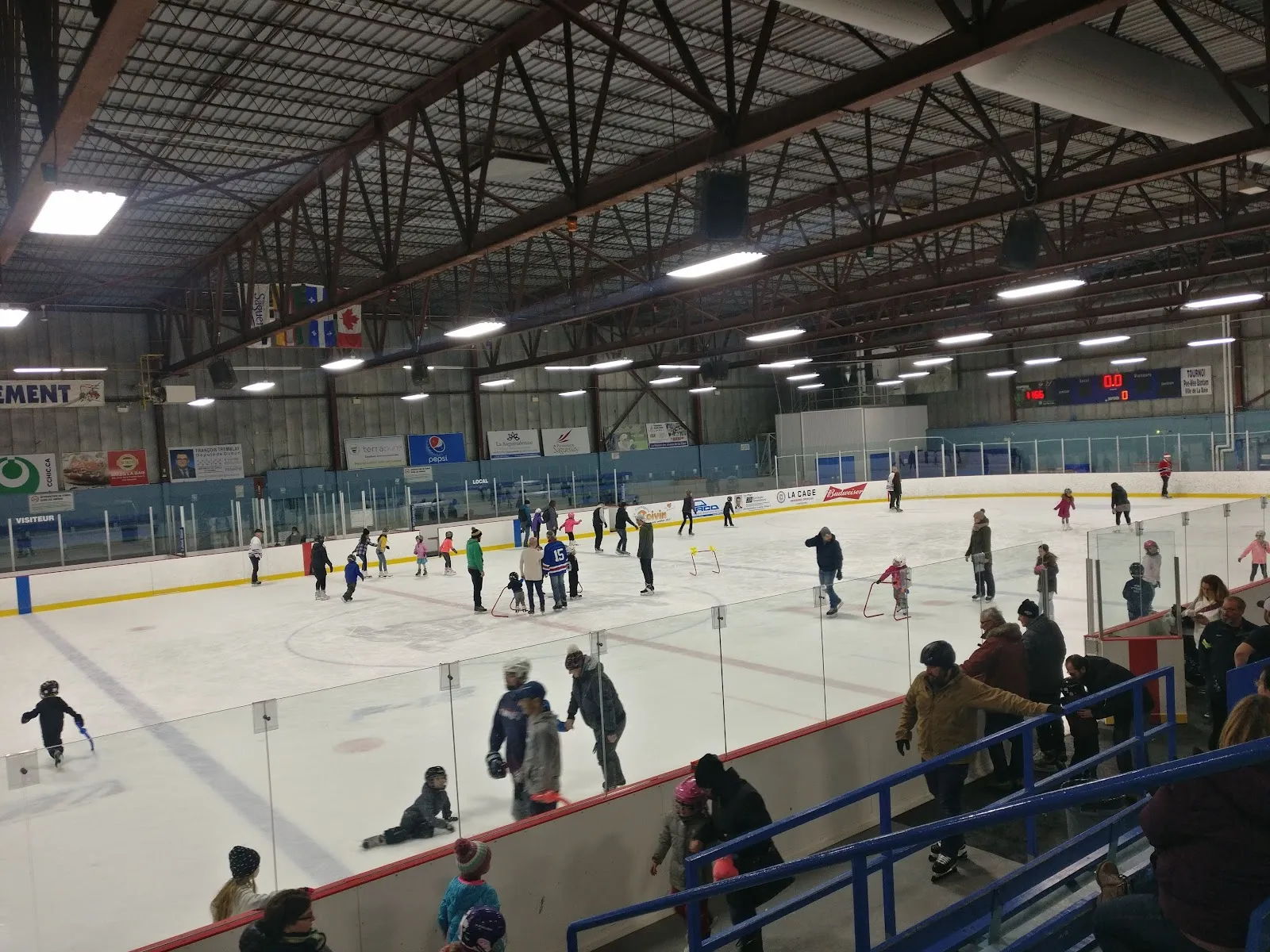 A busy public skating session on the ice at the Centre des sports Jean-Claude-Tremblay in La Baie, seen from the rail — Centre des sports Jean-Claude-Tremblay
