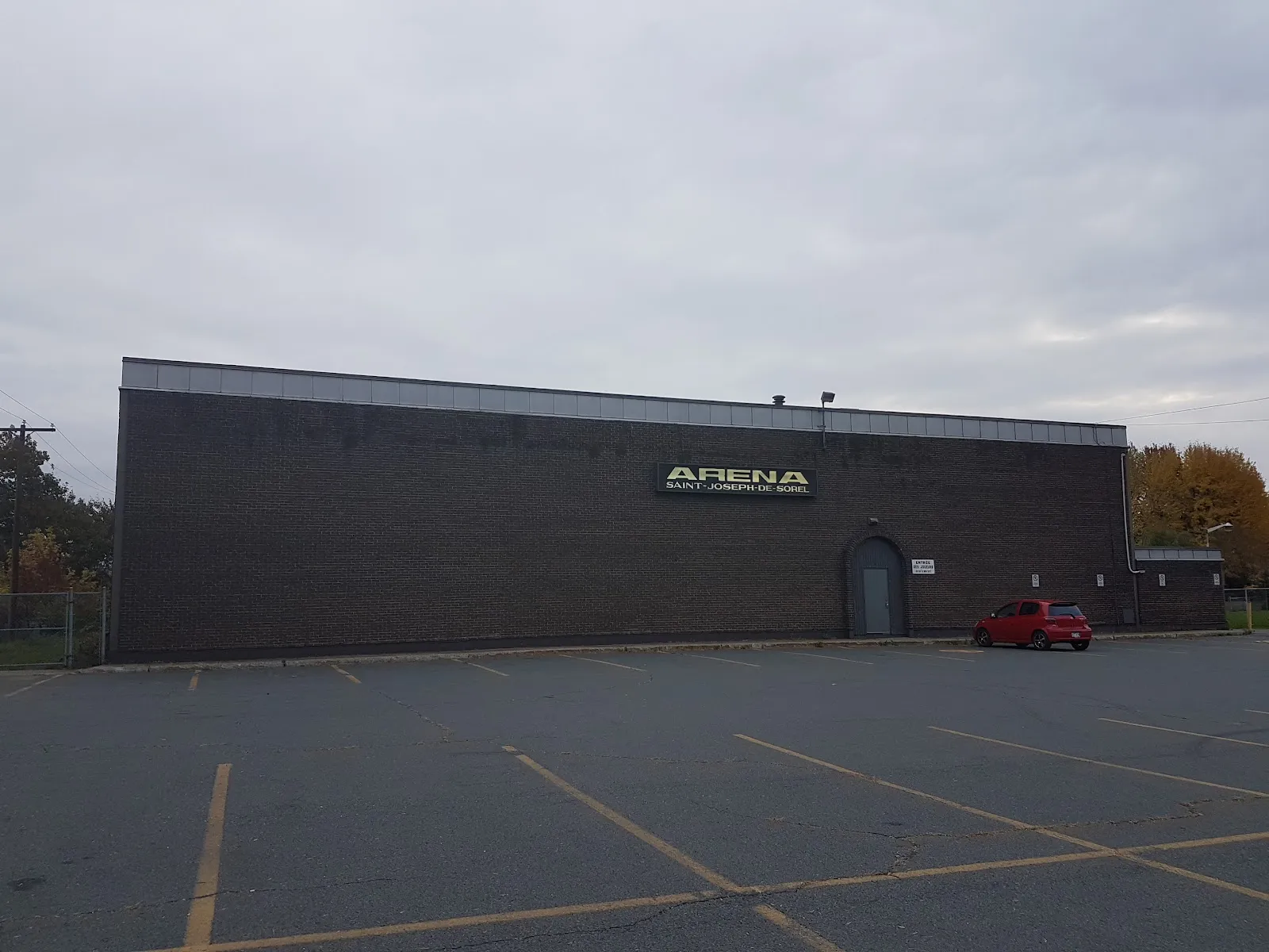 The dark brick side of the Aussant arena with the Arena Saint-Joseph-de-Sorel sign above the door — Centre récréatif Aussant (Aréna)