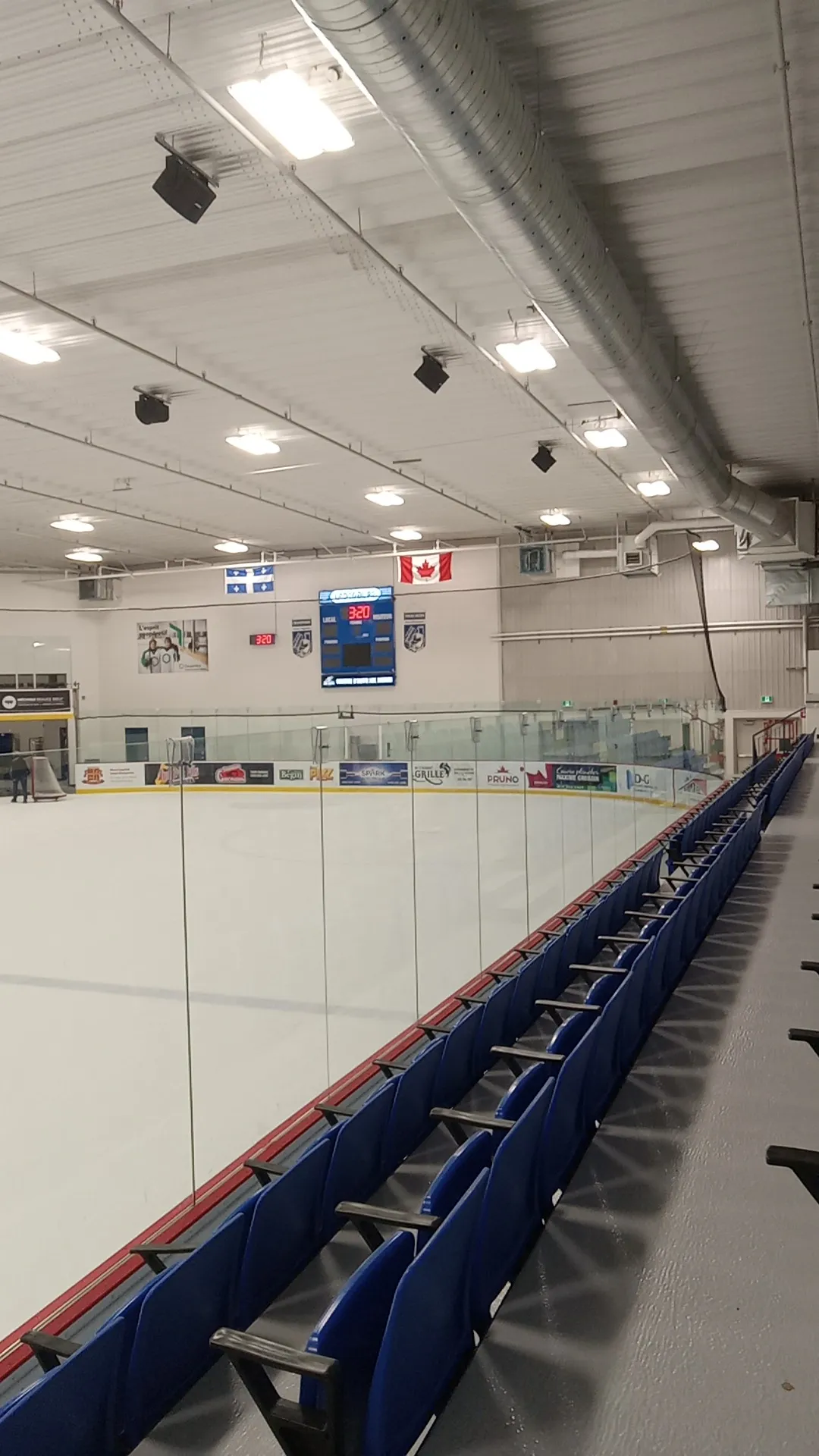 La glace vide du Centre récréatif Desjardins à Saint-Prosper, avec des sièges bleus le long de la baie vitrée et le drapeau du Québec sur le mur du fond — Centre récréatif Desjardins de Saint-Prosper