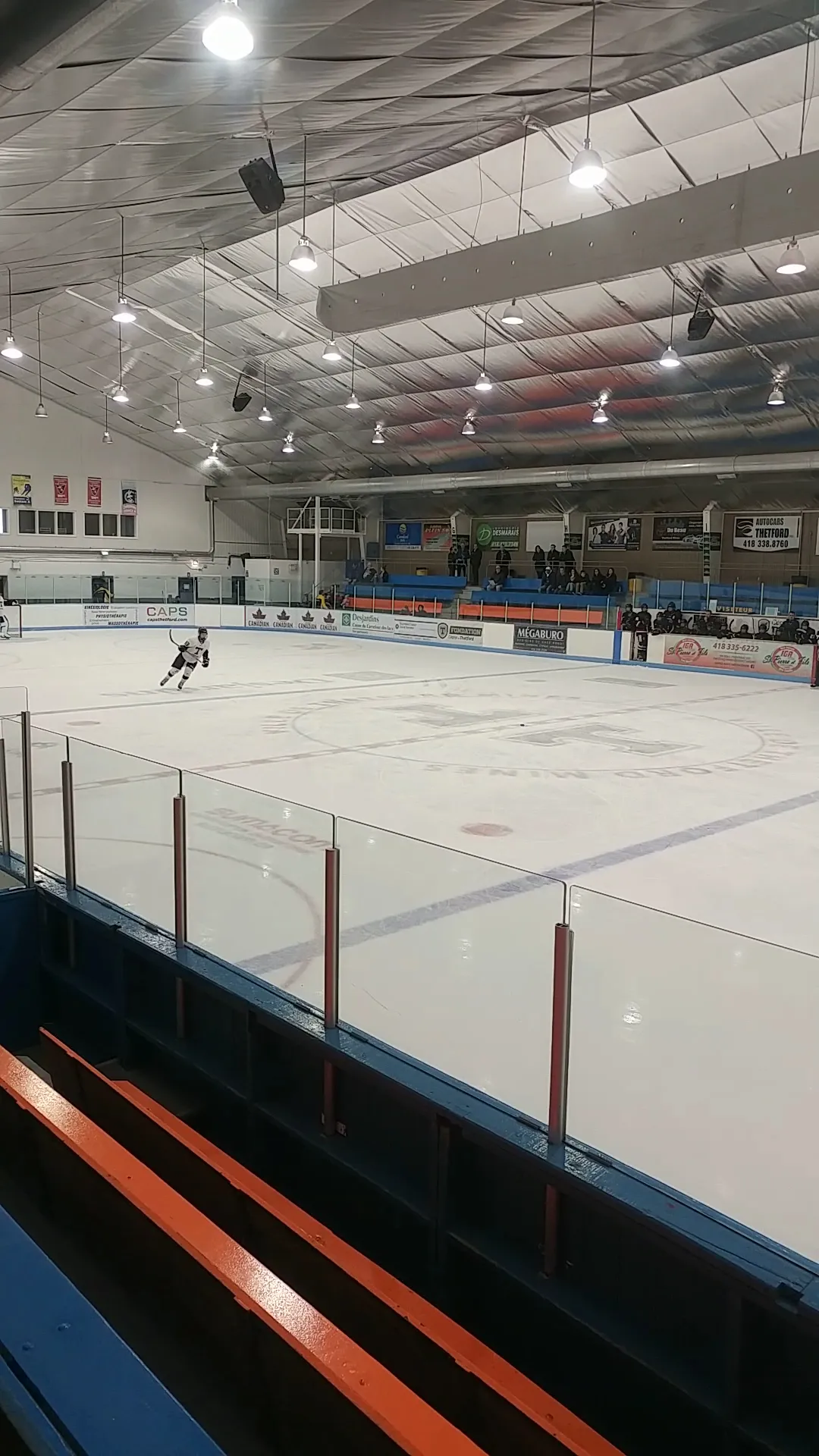 La glace de l’aréna de Thetford Mines vue des gradins, avec un seul patineur au loin sur la surface et des bannières le long du mur du fond — Centre Renaud-Fournier