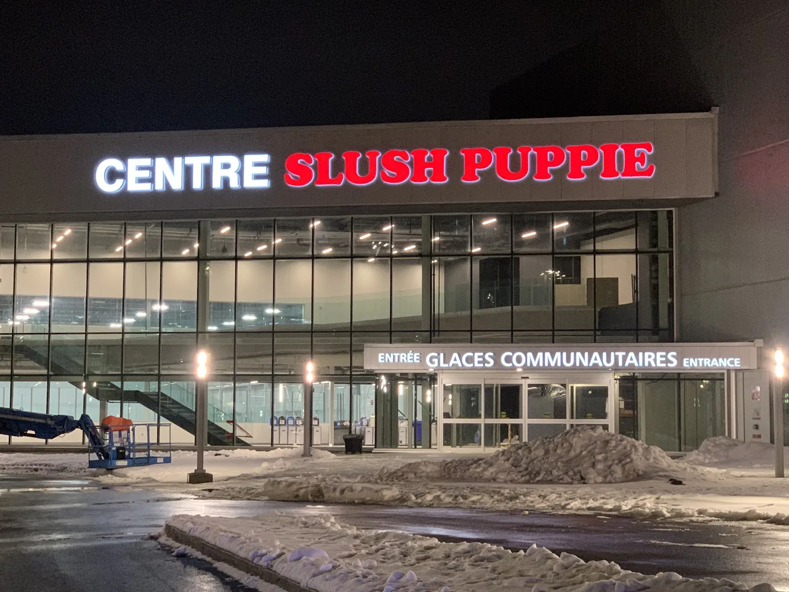 The glass front lit up at night under the Centre Slush Puppie sign, with the separate community-rinks entrance (Entrée glaces communautaires) at right. — Centre Slush Puppie