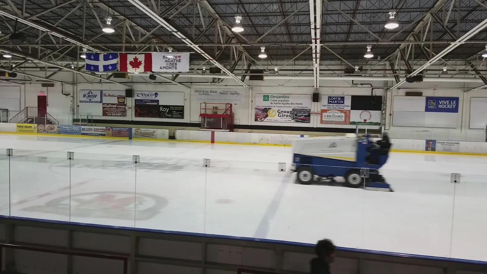 The ice resurfacer on the ice of the Centre sportif Damien-Hétu, with the stands and flags beyond — Centre sportif Damien-Hétu