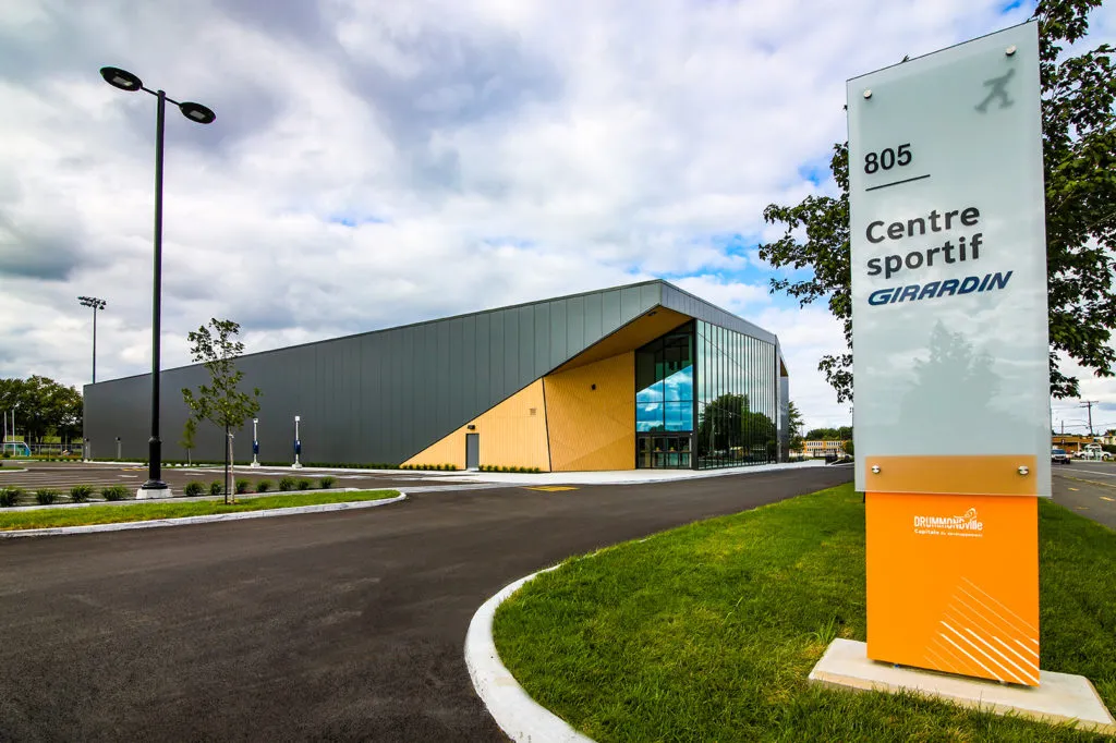 The Centre sportif Girardin seen from the car park: a dark-clad building with a glass entrance and its sign. — Centre sportif Girardin