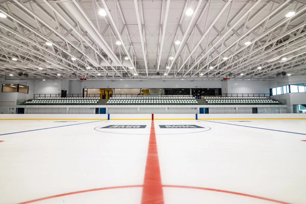 The ice sheet at the Centre sportif Girardin, with a bank of seats along the far side and the blue lines and centre circle marked. — Centre sportif Girardin