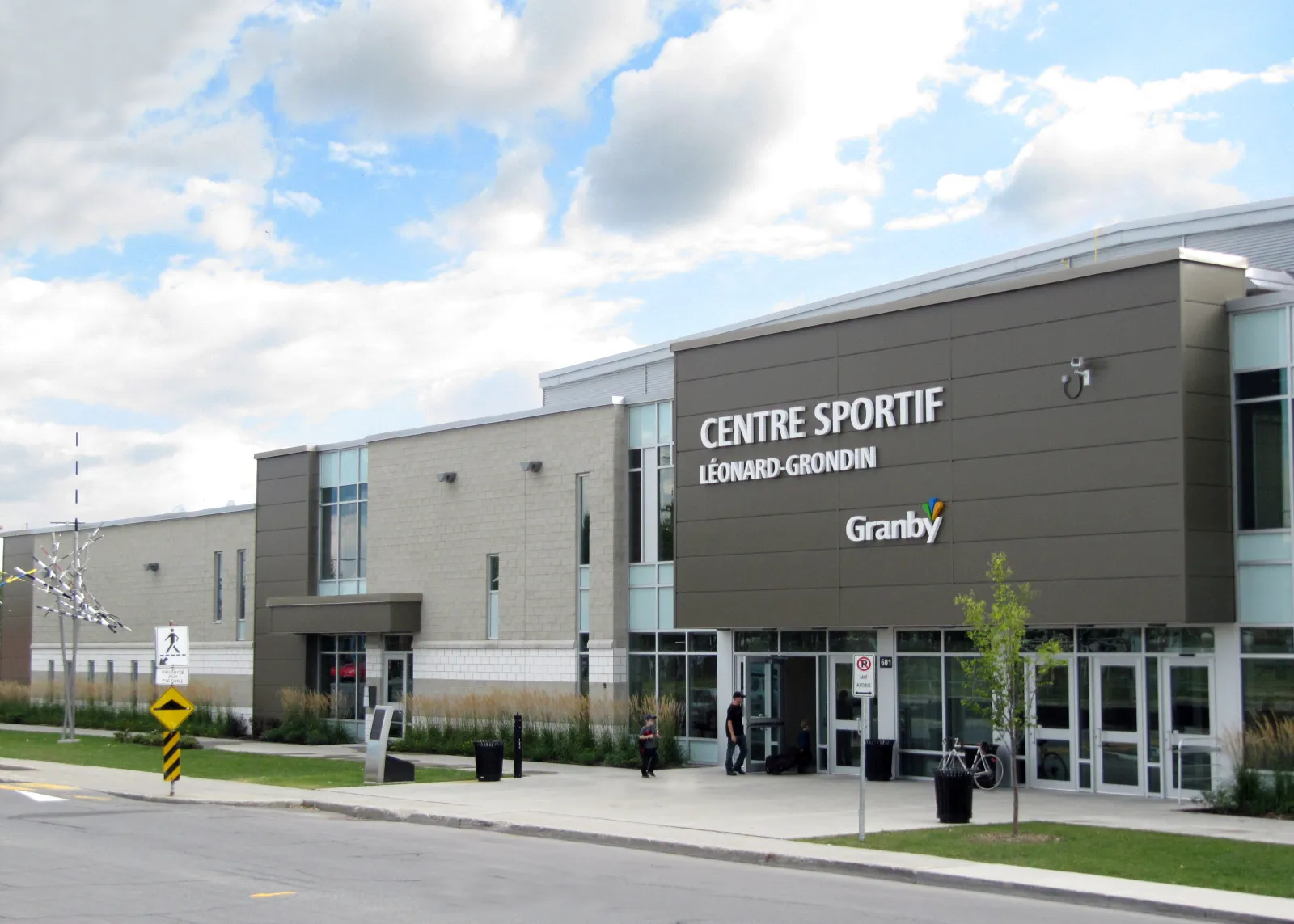 The main entrance under a grey panelled block lettered Centre sportif Léonard-Grondin and Granby, with the long low wing of the arena behind it. — Centre sportif Léonard-Grondin