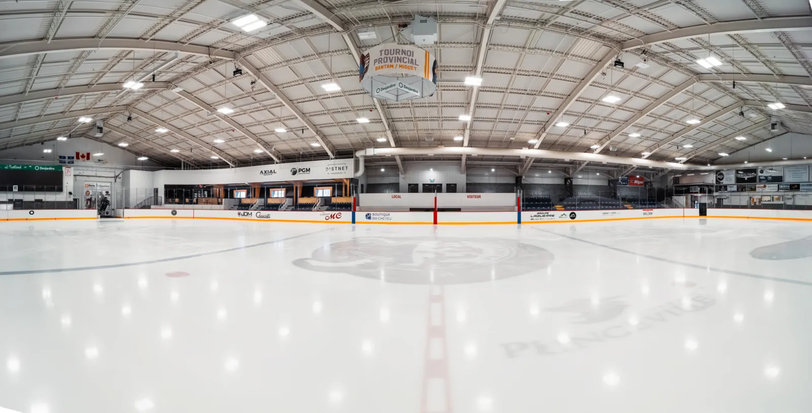The renovated rink from centre ice, with a white steel-truss roof and the stands along the far side. — Centre sportif Paul-de-la-Sablonnière