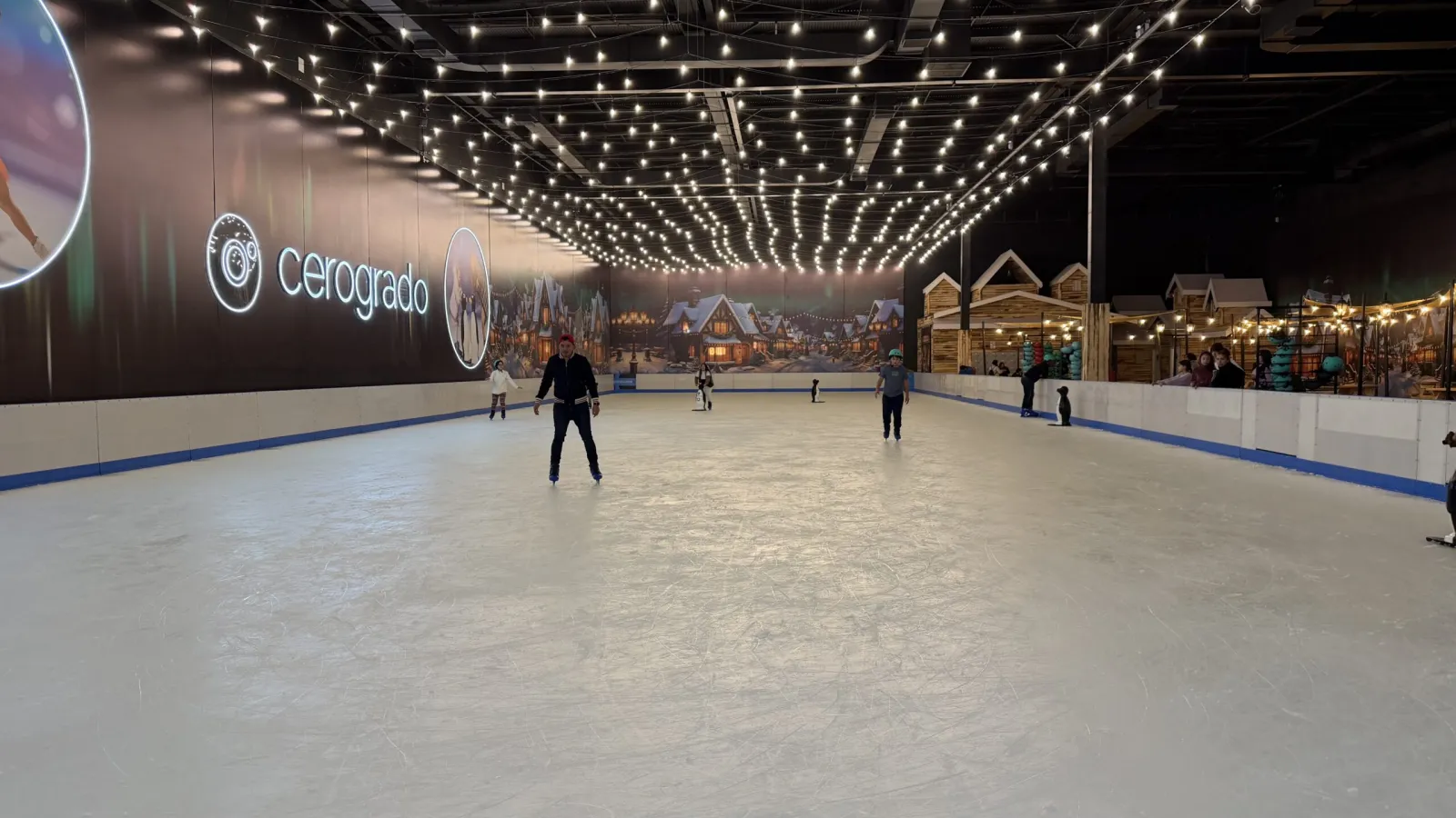 La pista de hielo bajo el cielo raso con luces de cadena, con el mural de la pared de Cerogrado y algunos patinadores — Cerogrado La Florida (Santa Amalia)