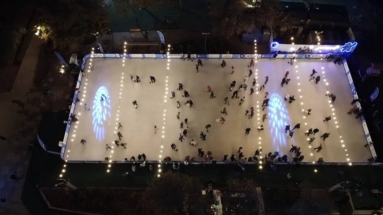 The lit open-air rink in Parque Araucano seen from above at night, with skaters spread across the ice — Cerogrado Parque Araucano (Las Condes)